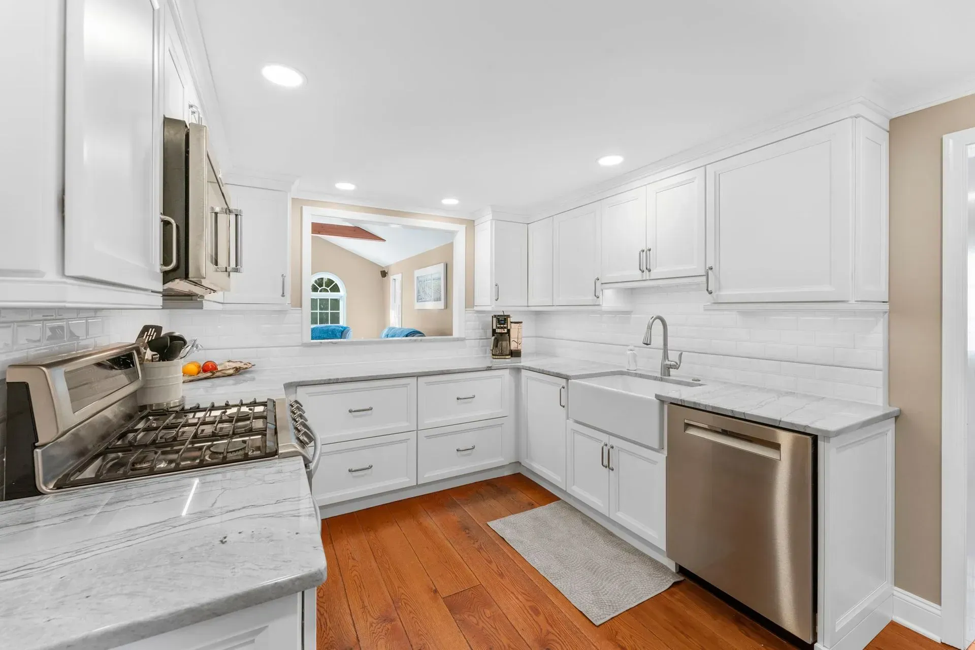Bright white kitchen with stainless steel appliances, marble counters, and warm wood flooring  In Bucks County PA