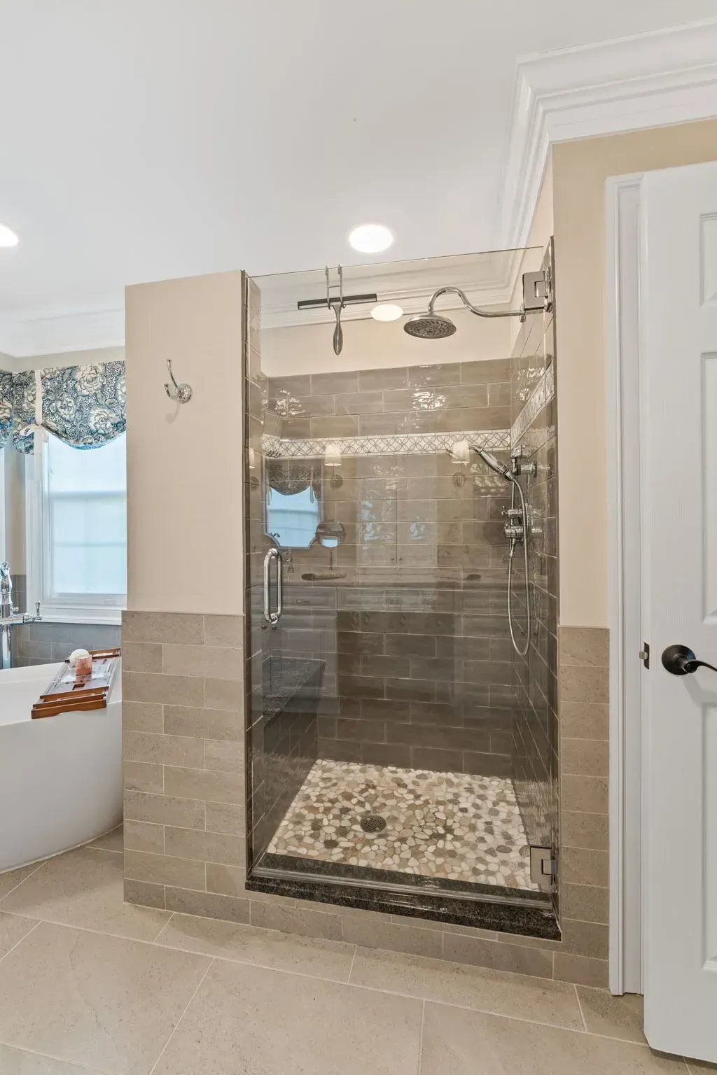 Bathroom with a glass-enclosed shower, beige tile, and white vanity next to a bedroom window In Bucks County PA
