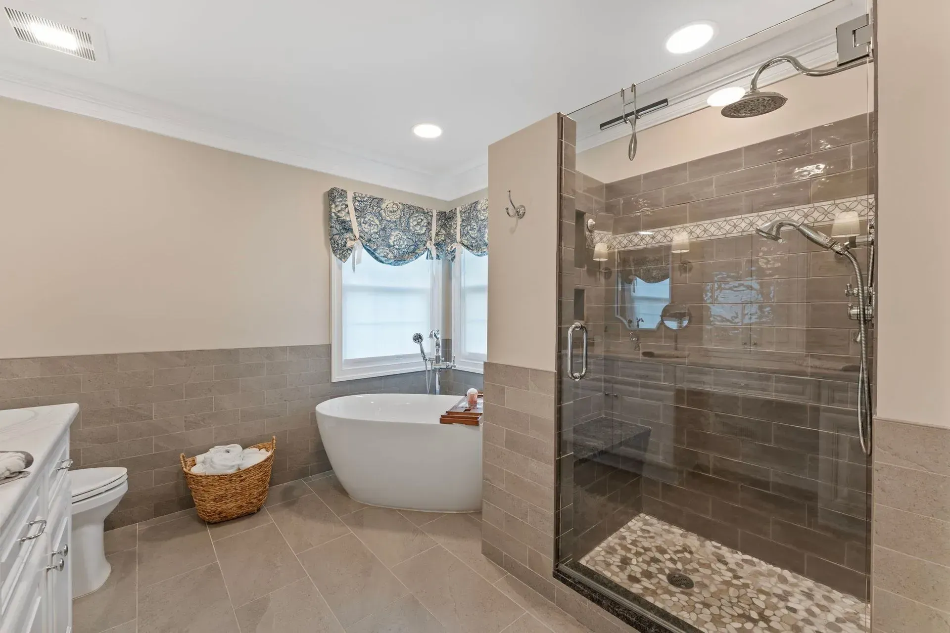Modern bathroom with a freestanding tub, walk-in glass shower, and wicker basket under a window with drapes In Bucks County PA