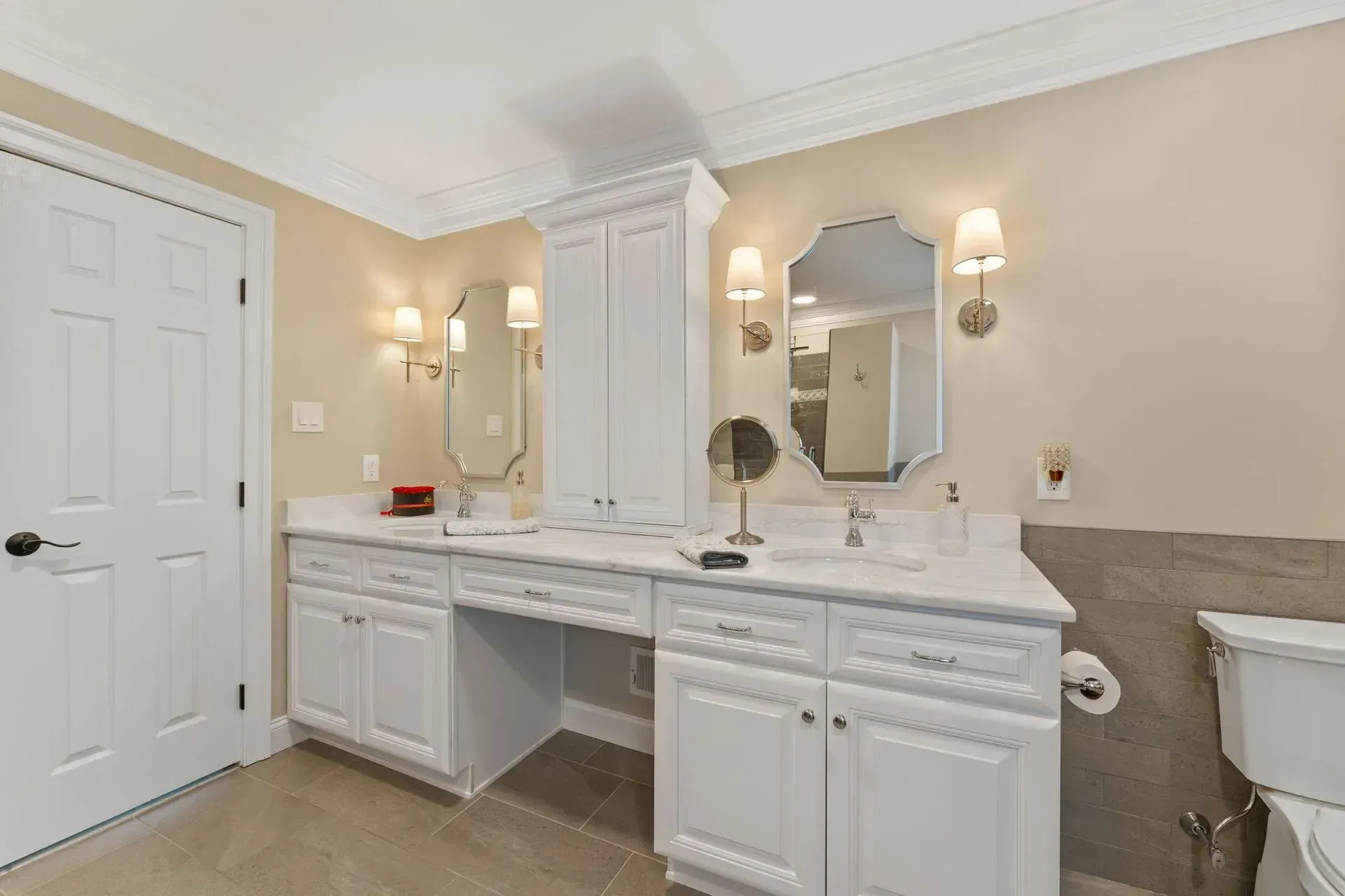 Elegant bathroom vanity with twin mirrors, white cabinetry, beige walls, and a bathtub at right In Bucks County PA