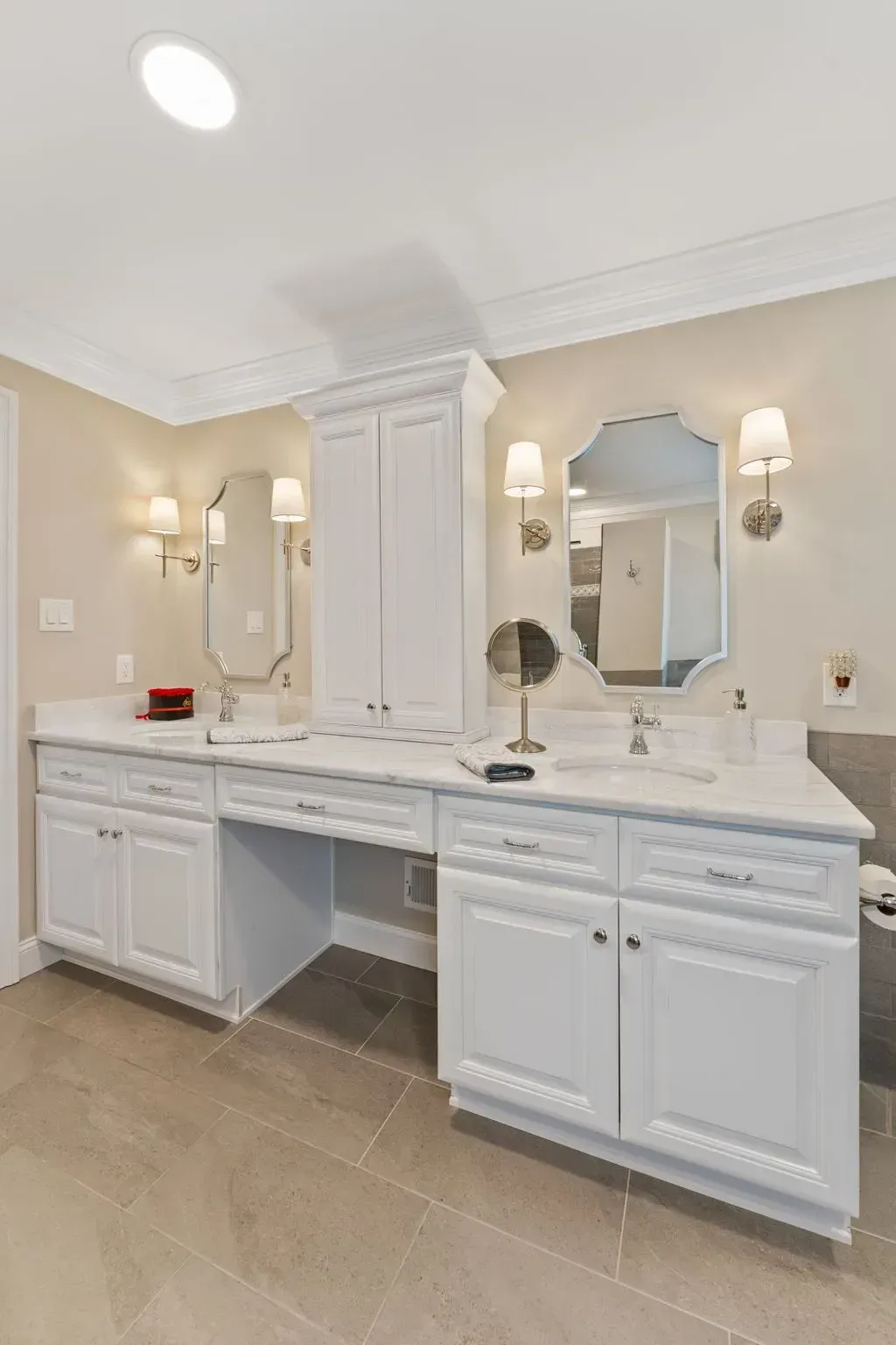 Bright bathroom vanity with white cabinets, marble countertop, mirrors, sconces, and beige tile floor In Bucks County PA