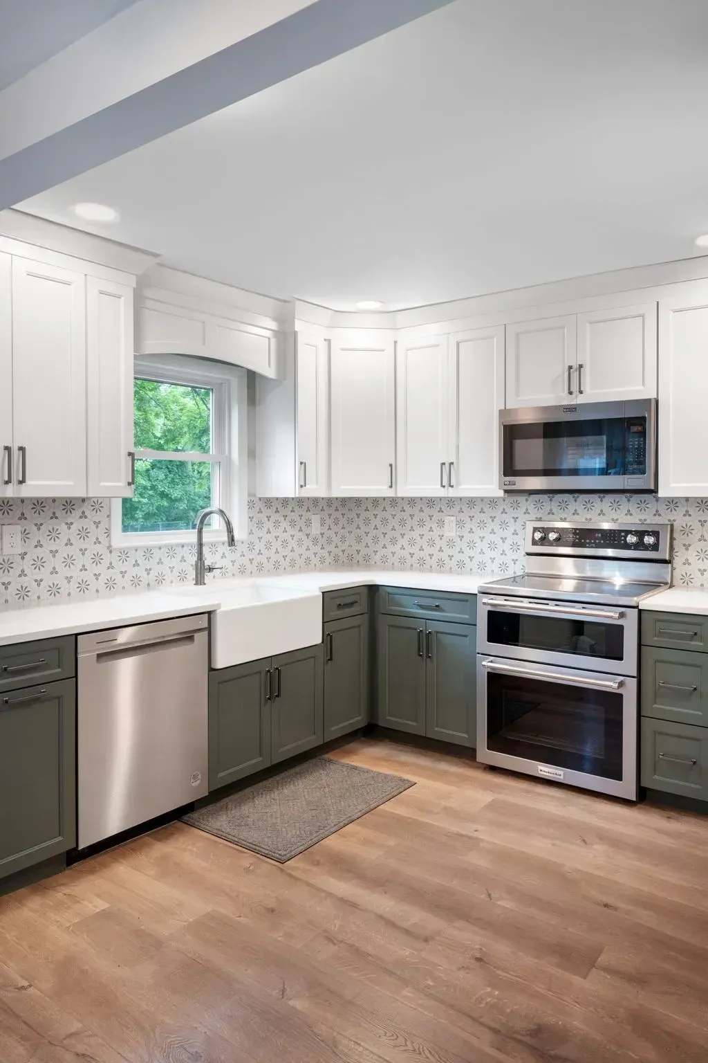 Bright white kitchen with gray lower cabinets, stainless appliances, wood floor, and a window over the sink  In Bucks County PA