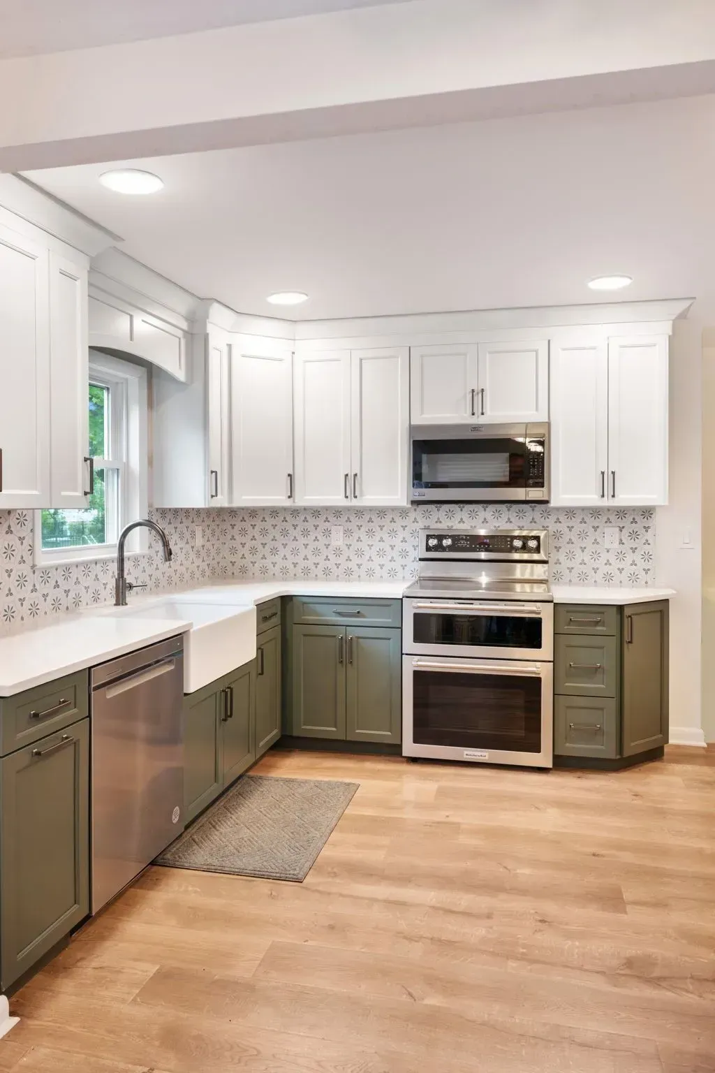 Bright white kitchen with stainless steel appliances, green lower cabinets, mosaic backsplash, and wood flooring  In Bucks County PA