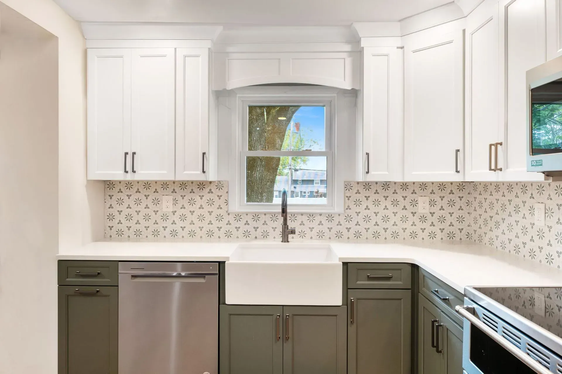 Bright kitchen with white cabinets, farmhouse sink, patterned backsplash, and stainless steel dishwasher  In Bucks County PA