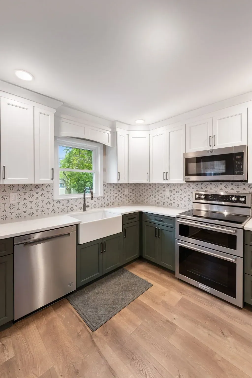 Bright white kitchen with stainless steel appliances, green lower cabinets, and a window over the sink  In Bucks County PA