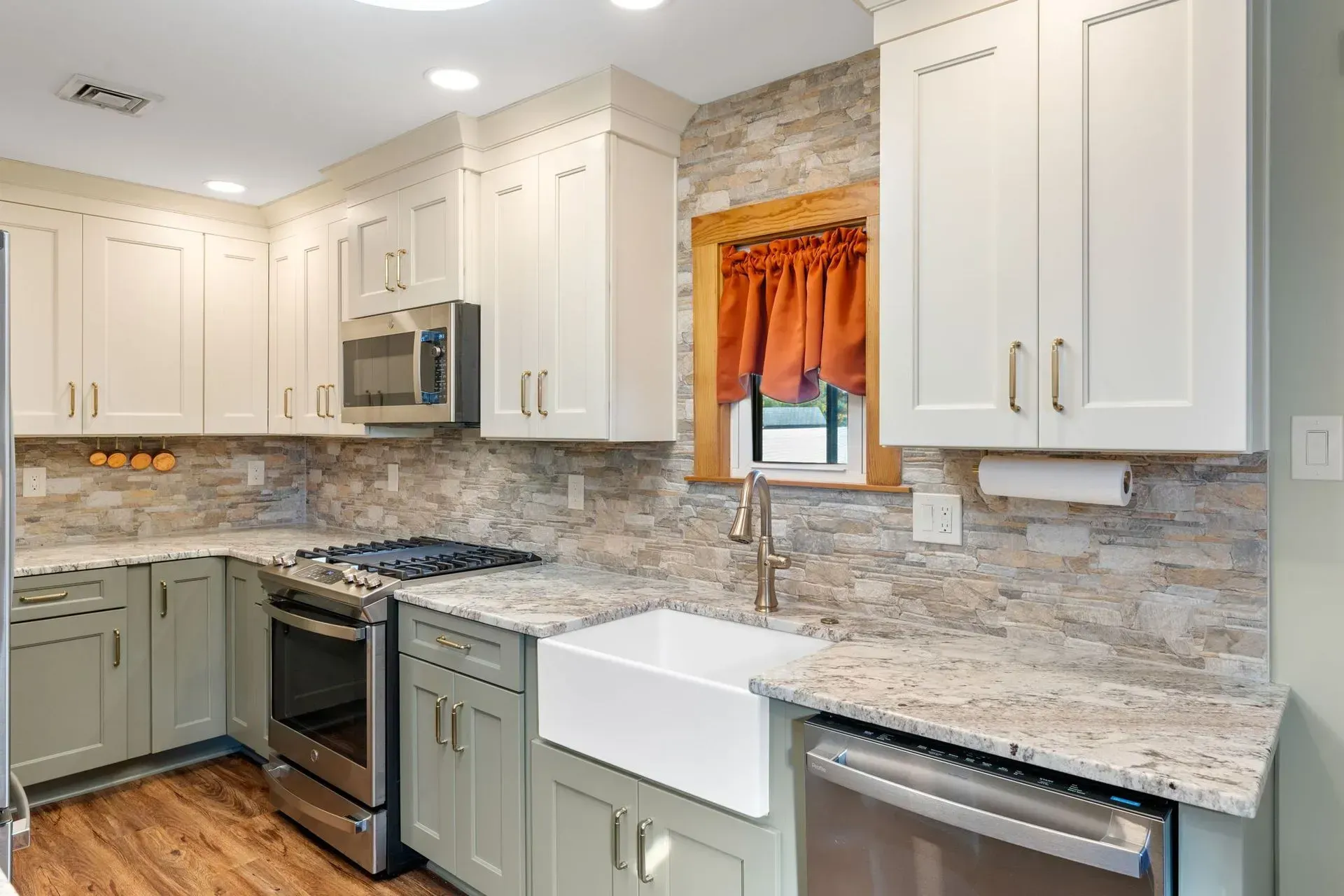 Modern kitchen with white cabinets, gray lower cabinets, granite counters, and a farmhouse sink by a window In Bucks County PA