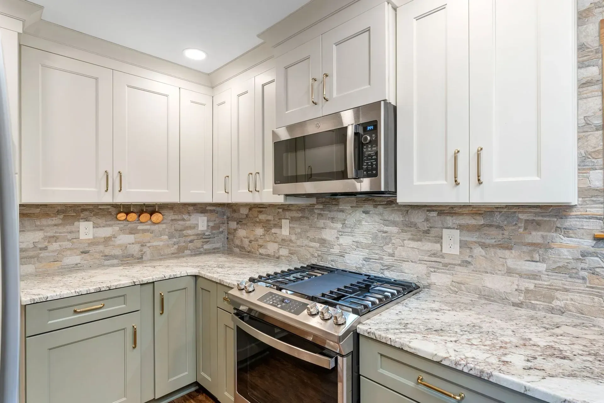 Bright modern kitchen with white cabinets, stone countertops, and stainless steel stove and microwave In Bucks County PA