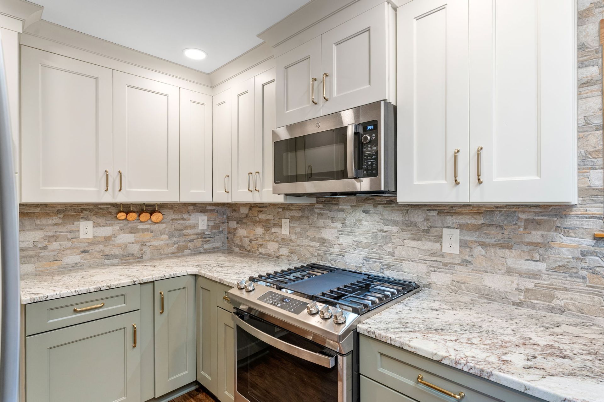 Modern kitchen with white cabinets, granite countertops, stainless steel microwave, and gas range IN Bucks Country PA