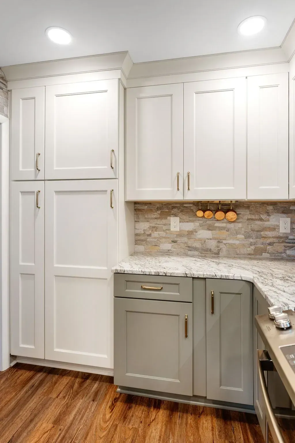 White kitchen with tall cabinets, gray lower cabinets, granite counter, tile backsplash, and wood floor In Bucks County PA
