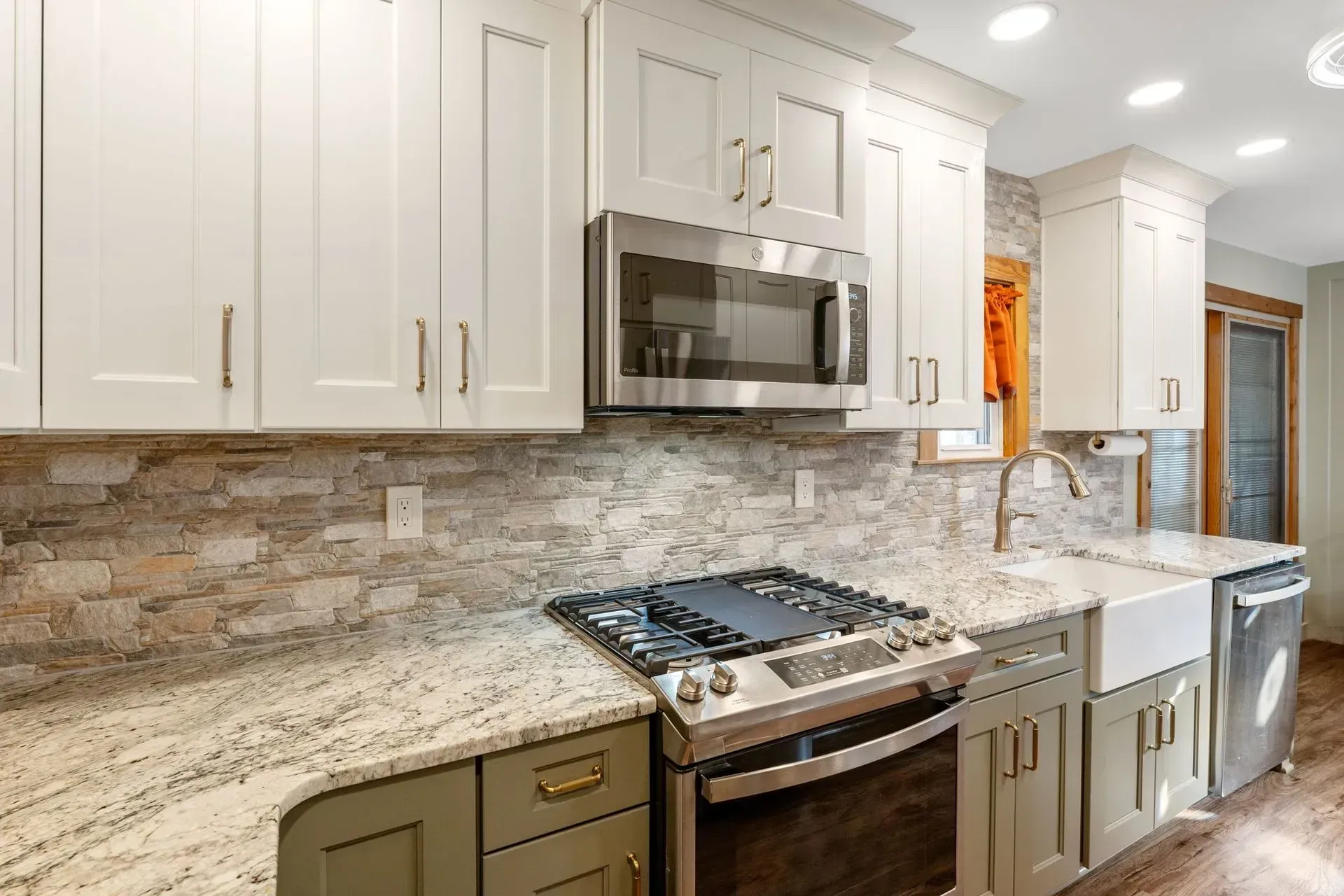 Bright modern kitchen with white cabinets, stone backsplash, stainless stove, microwave, and sink In Bucks County PA