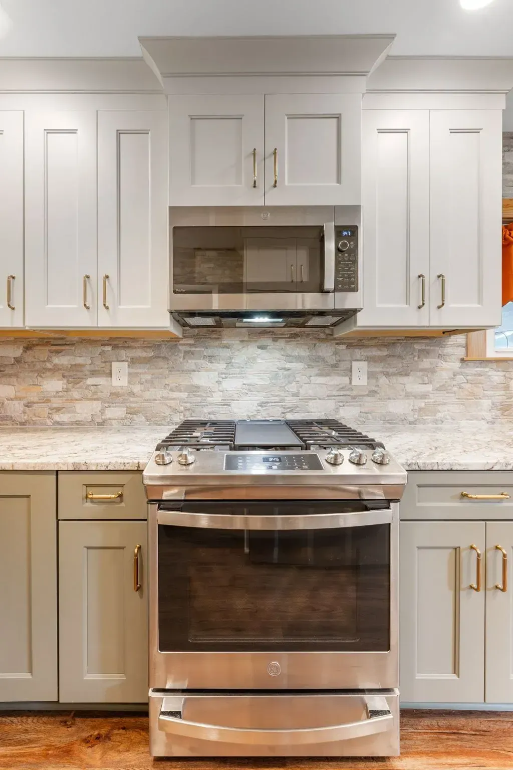 Modern kitchen with white cabinets, stainless steel stove and microwave, and a light stone backsplash In Bucks County PA