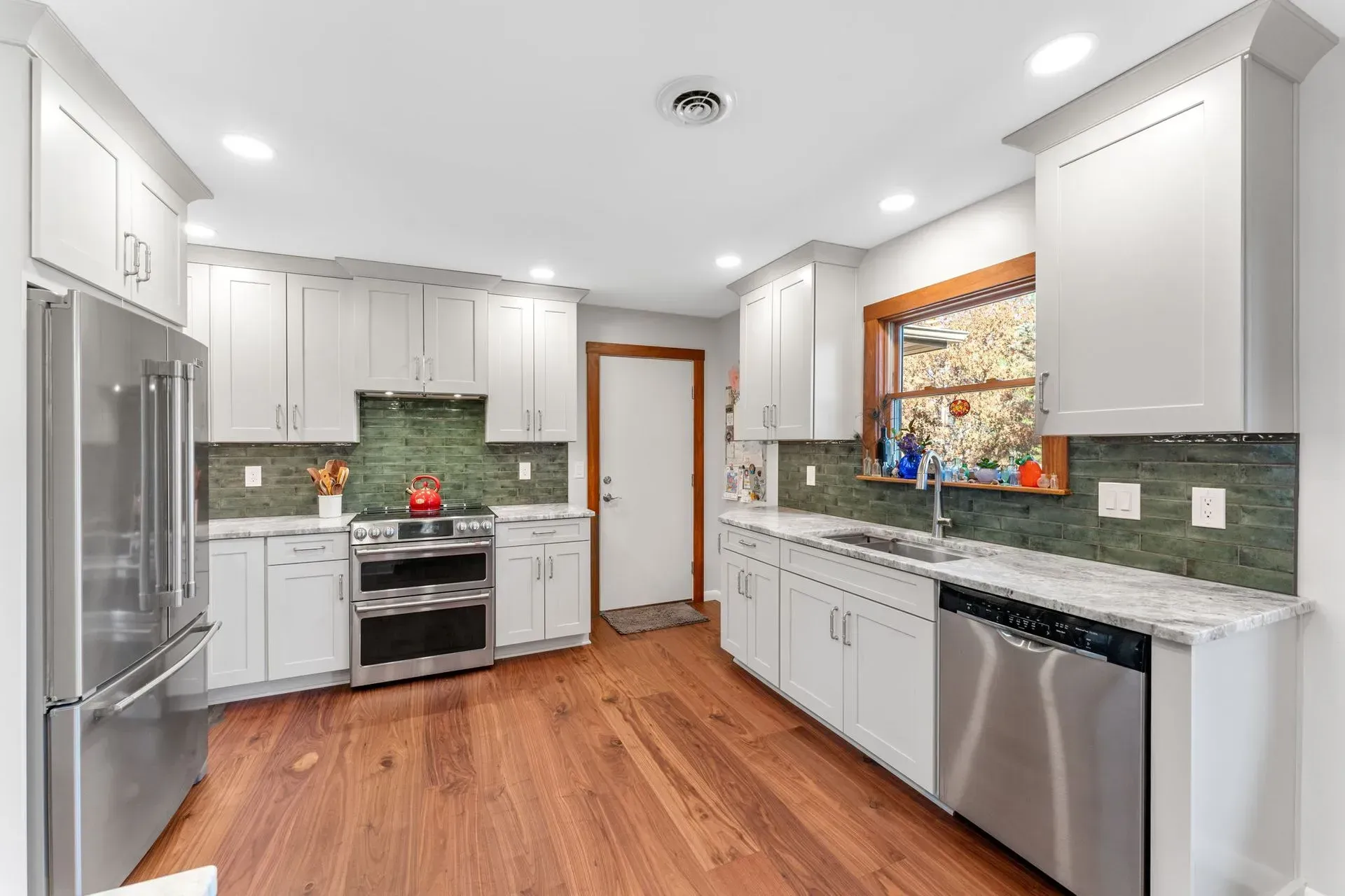 Bright modern kitchen with white cabinets, stainless appliances, green tile backsplash, and wood floors In Bucks Country PA