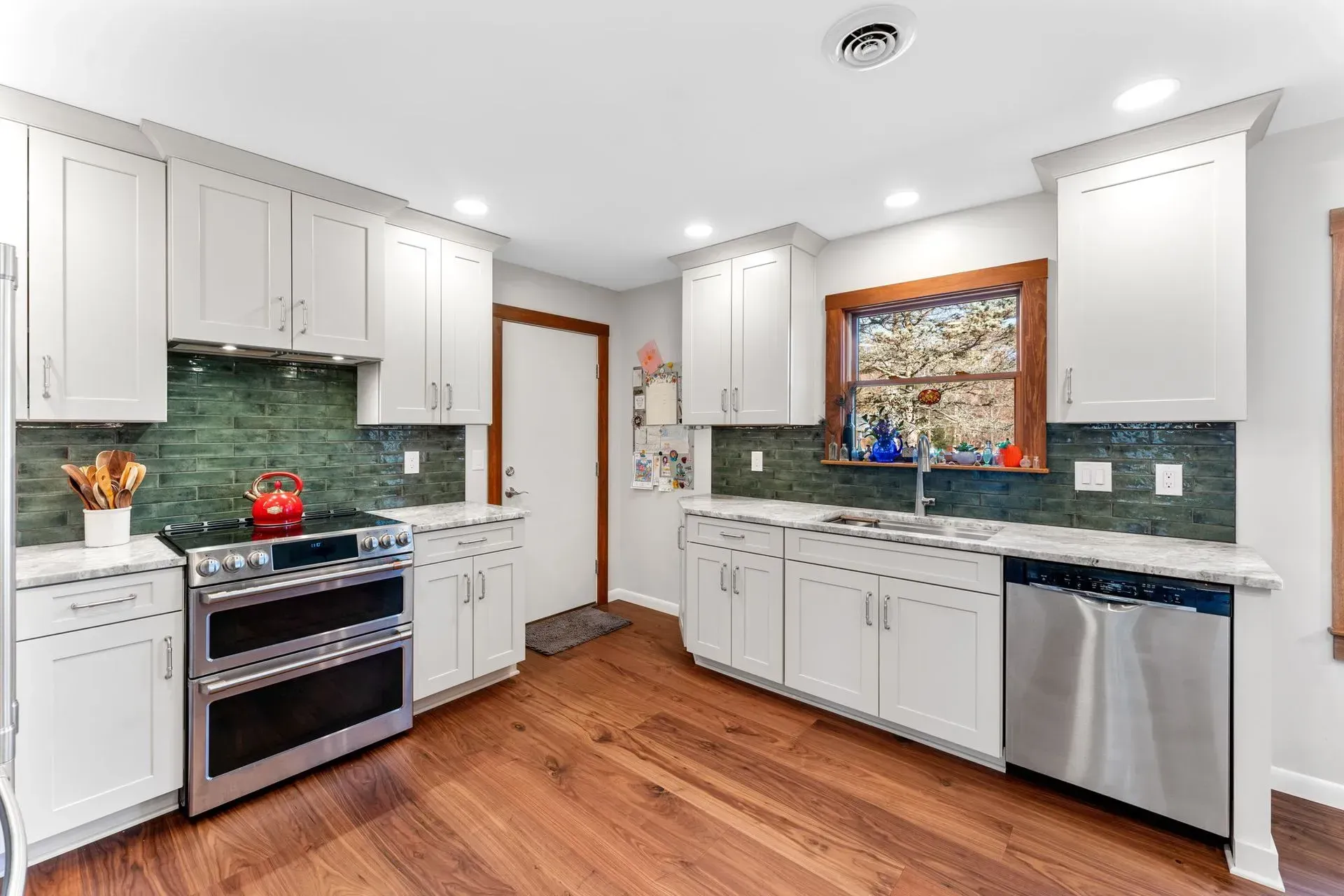 Bright white kitchen with green tile backsplash, hardwood floors, and stainless steel appliances In Bucks Country PA
