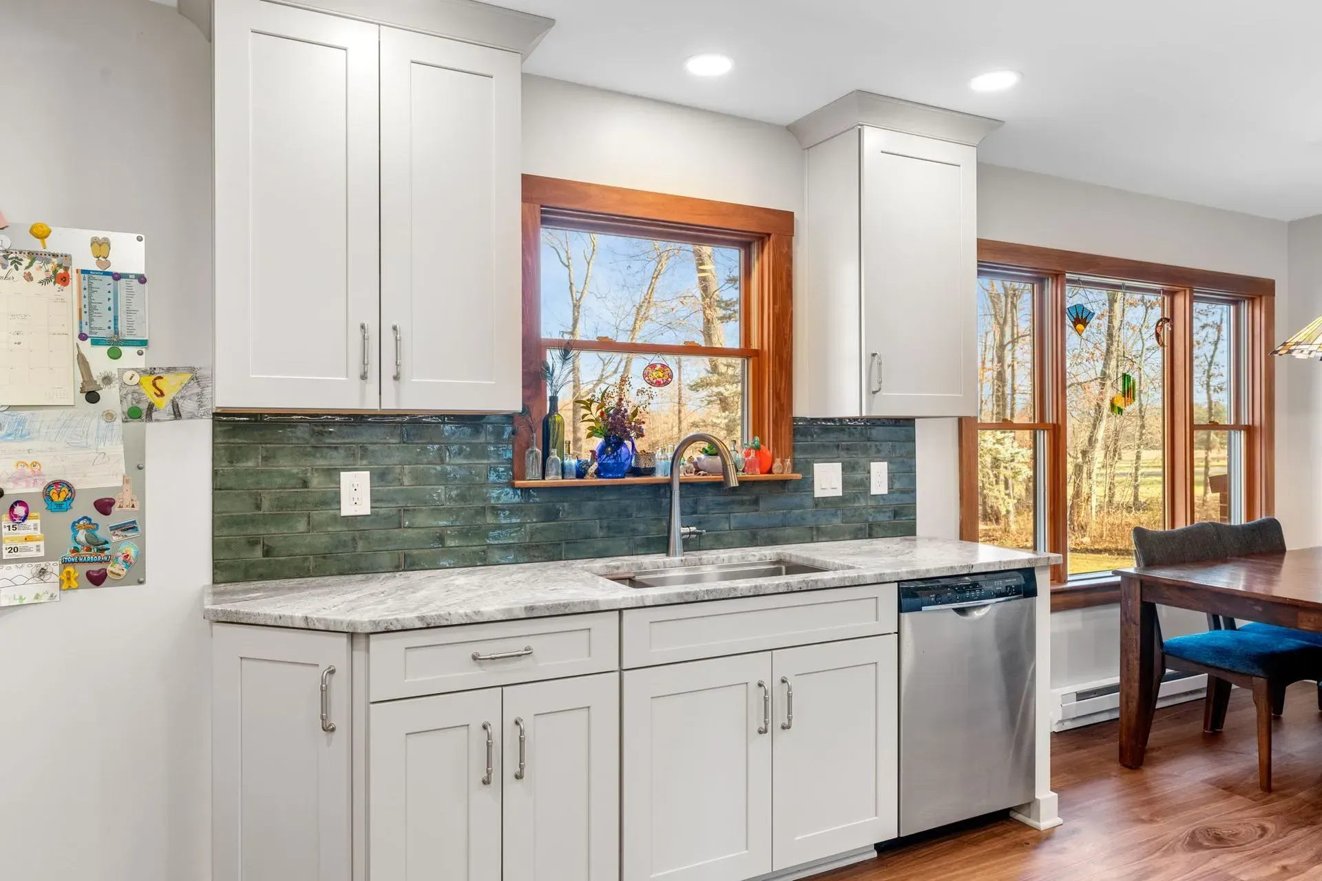 Bright kitchen with white cabinets, green tile backsplash, granite counters, and a dining table by windows.