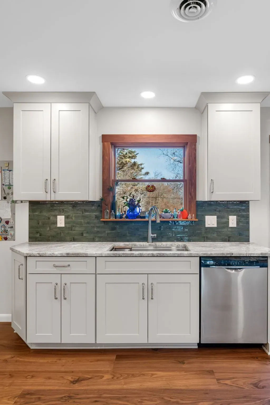 Bright kitchen with white cabinets, green tile backsplash, stainless dishwasher, and a window over the sink In Bucks Country PA