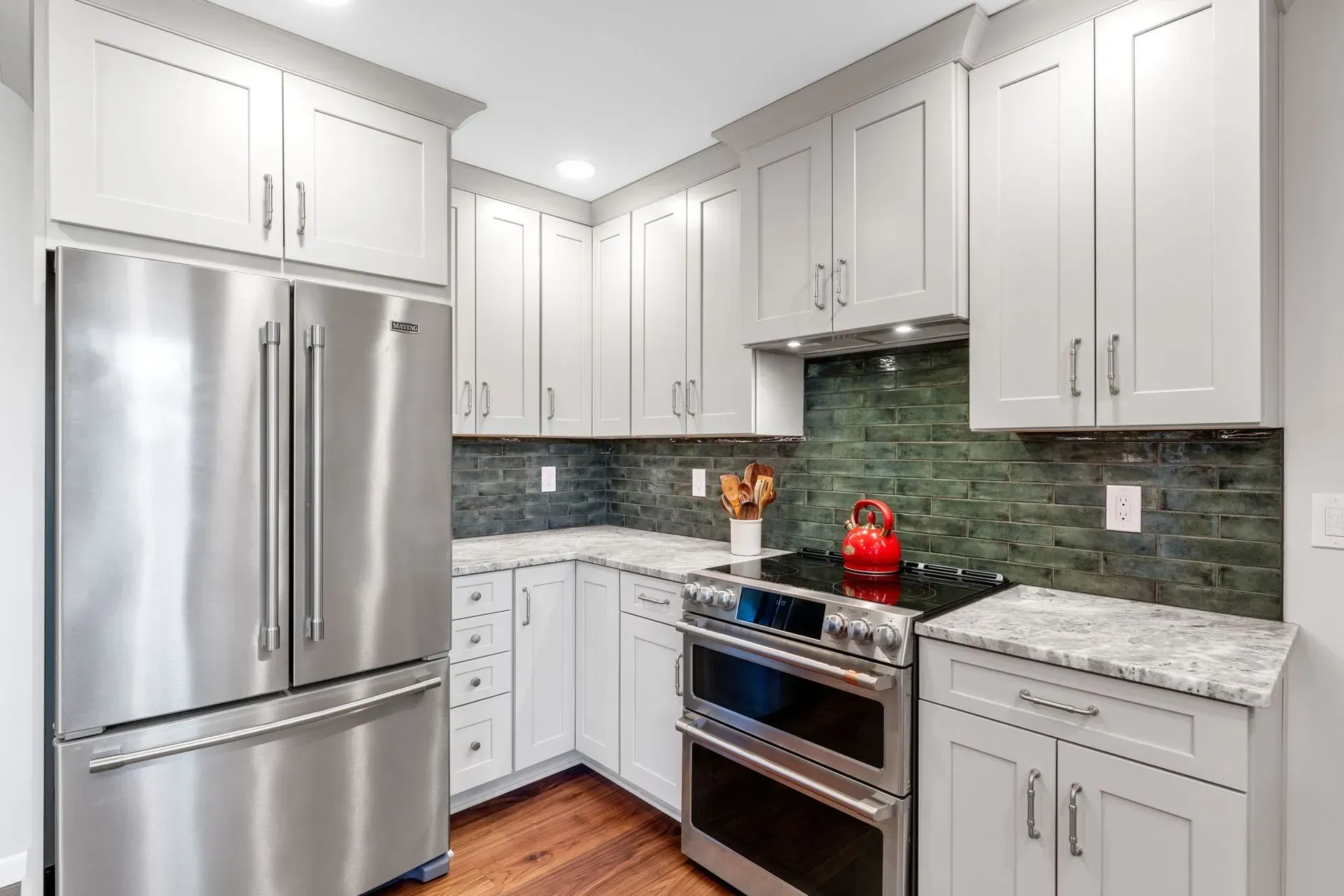 Modern kitchen with white cabinets, stainless steel appliances, green tile backsplash, and granite countertops In Bucks Country PA