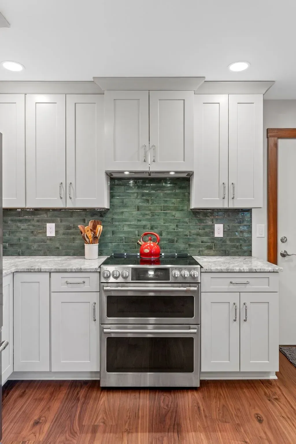 Modern kitchen with white cabinets, green tile backsplash, stainless stove, and red kettle In Bucks Country PA