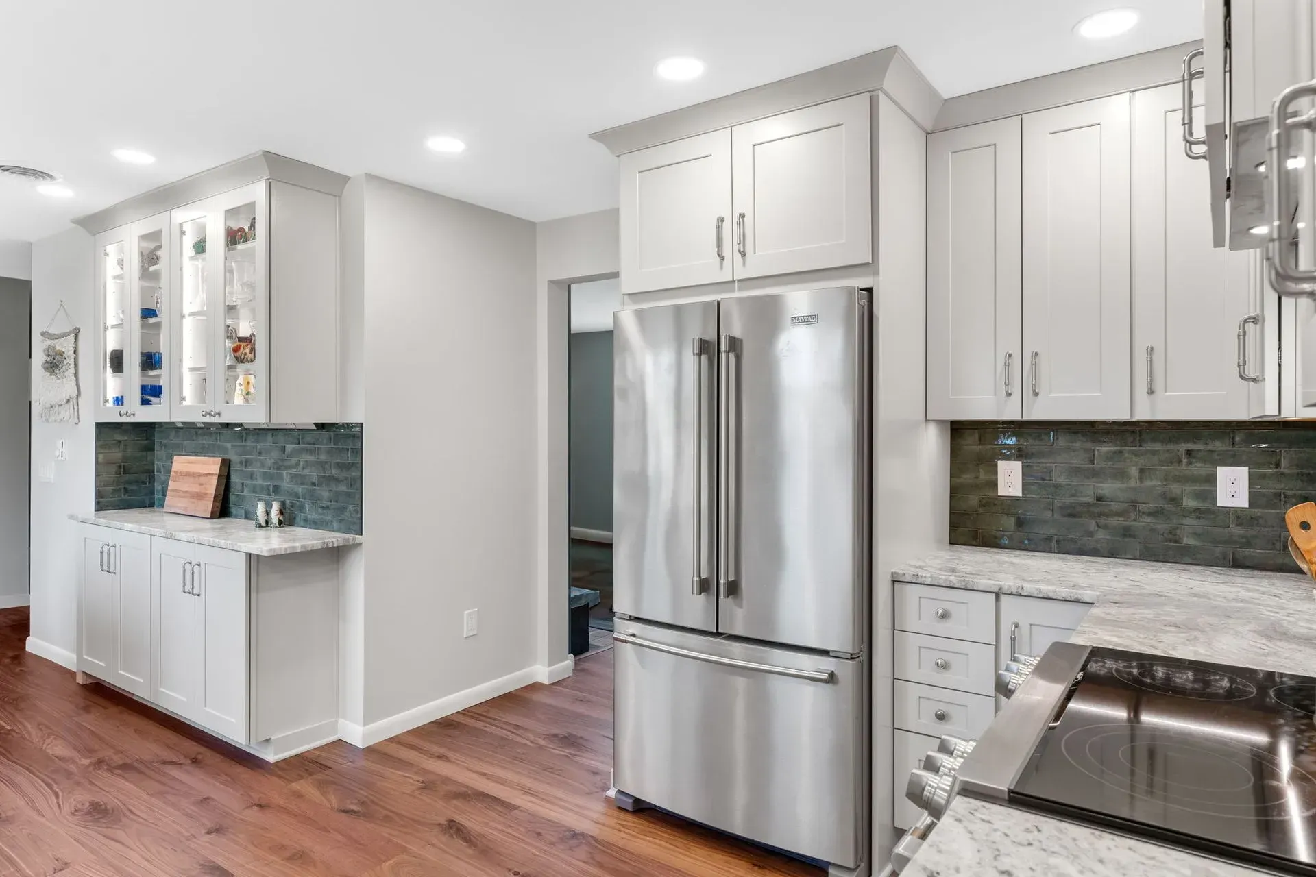 Modern white kitchen with stainless steel appliances, gray backsplash, and hardwood floors In Bucks Country PA