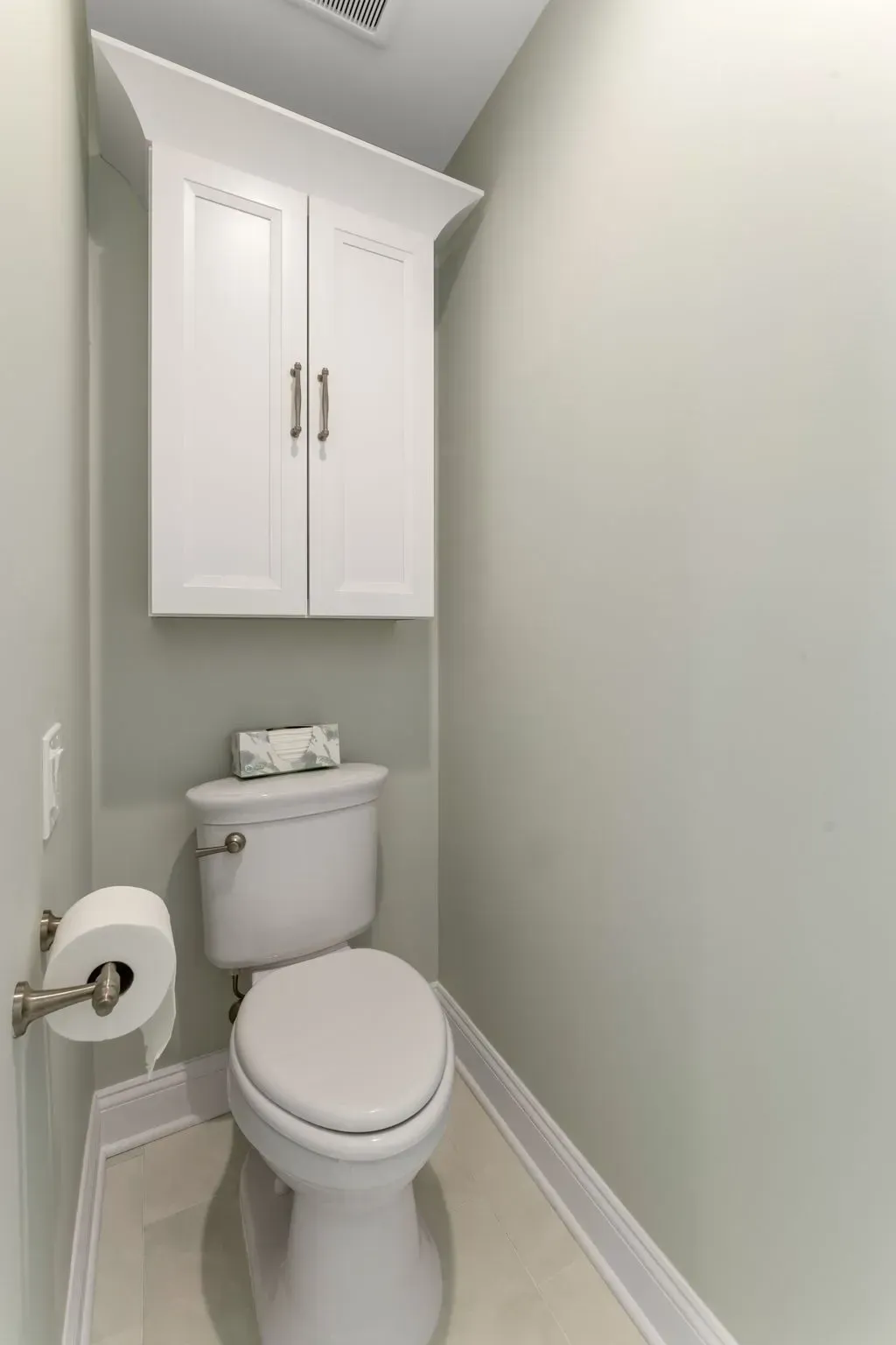 Small narrow bathroom with a white toilet, wall cabinet, and pale green walls In Bucks County PA