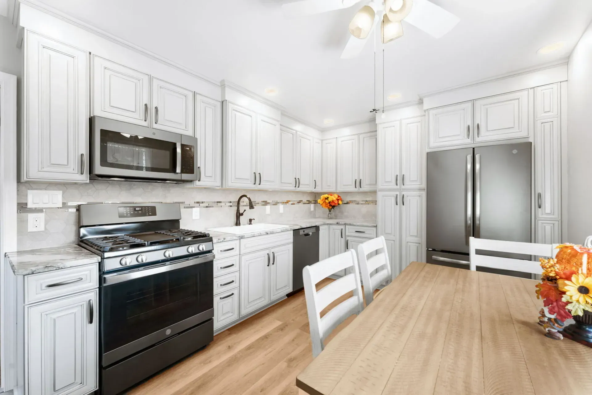 Bright white kitchen with stainless steel appliances and a wooden dining table in the foreground  In Bucks County PA