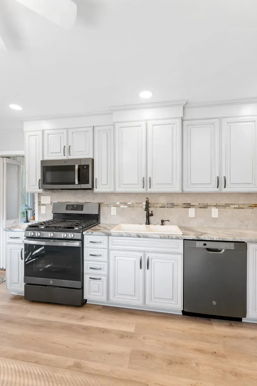 Bright kitchen with white cabinets, black stove and microwave, stainless dishwasher, and light wood floor  In Bucks County PA
