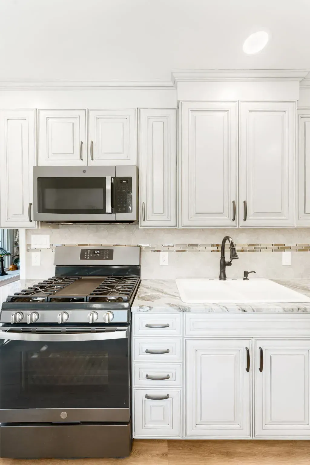 Bright white kitchen with stainless steel stove, microwave, cabinets, and sink with faucet  In Bucks County PA