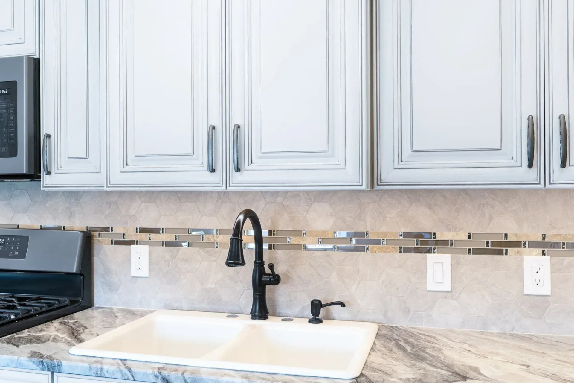 Bright kitchen sink with black faucet, white cabinets, beige tile backsplash, and granite countertop  In Bucks County PA