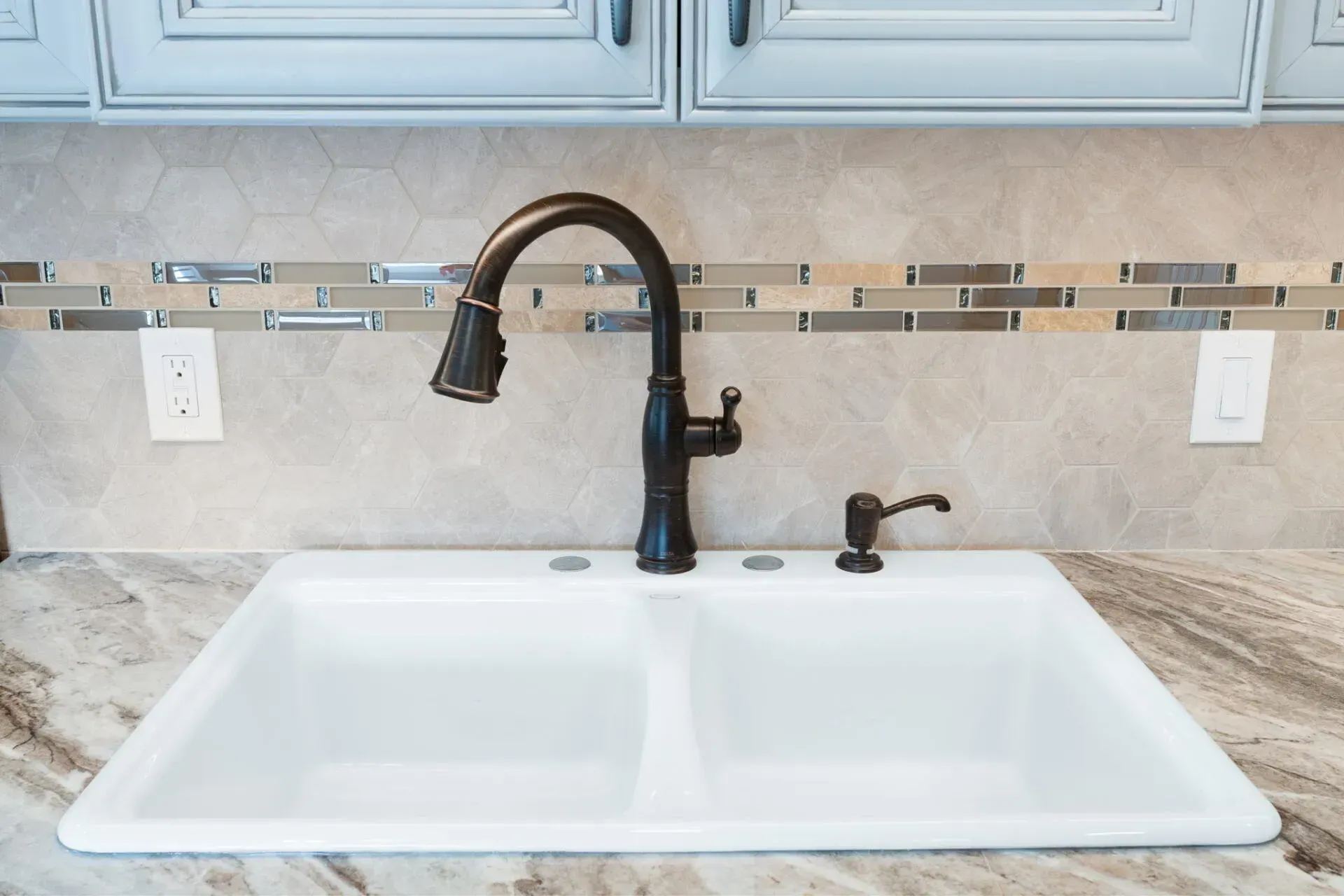 Kitchen sink with dark bronze faucet, white basin, and beige tile backsplash under light gray cabinets  In Bucks County PA