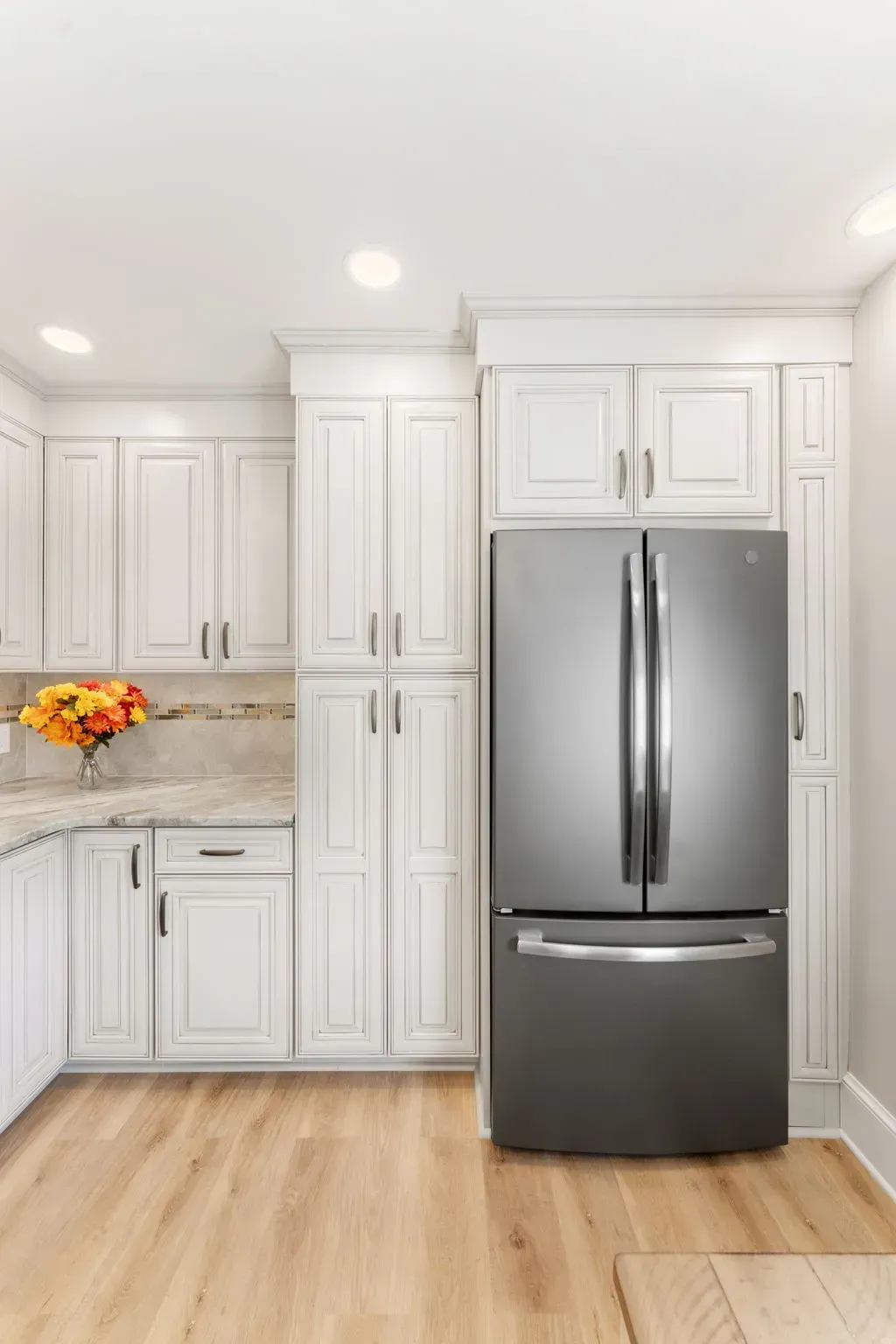 Modern white kitchen with stainless steel refrigerator, wood floors, and a vase of flowers on the counter  In Bucks County PA