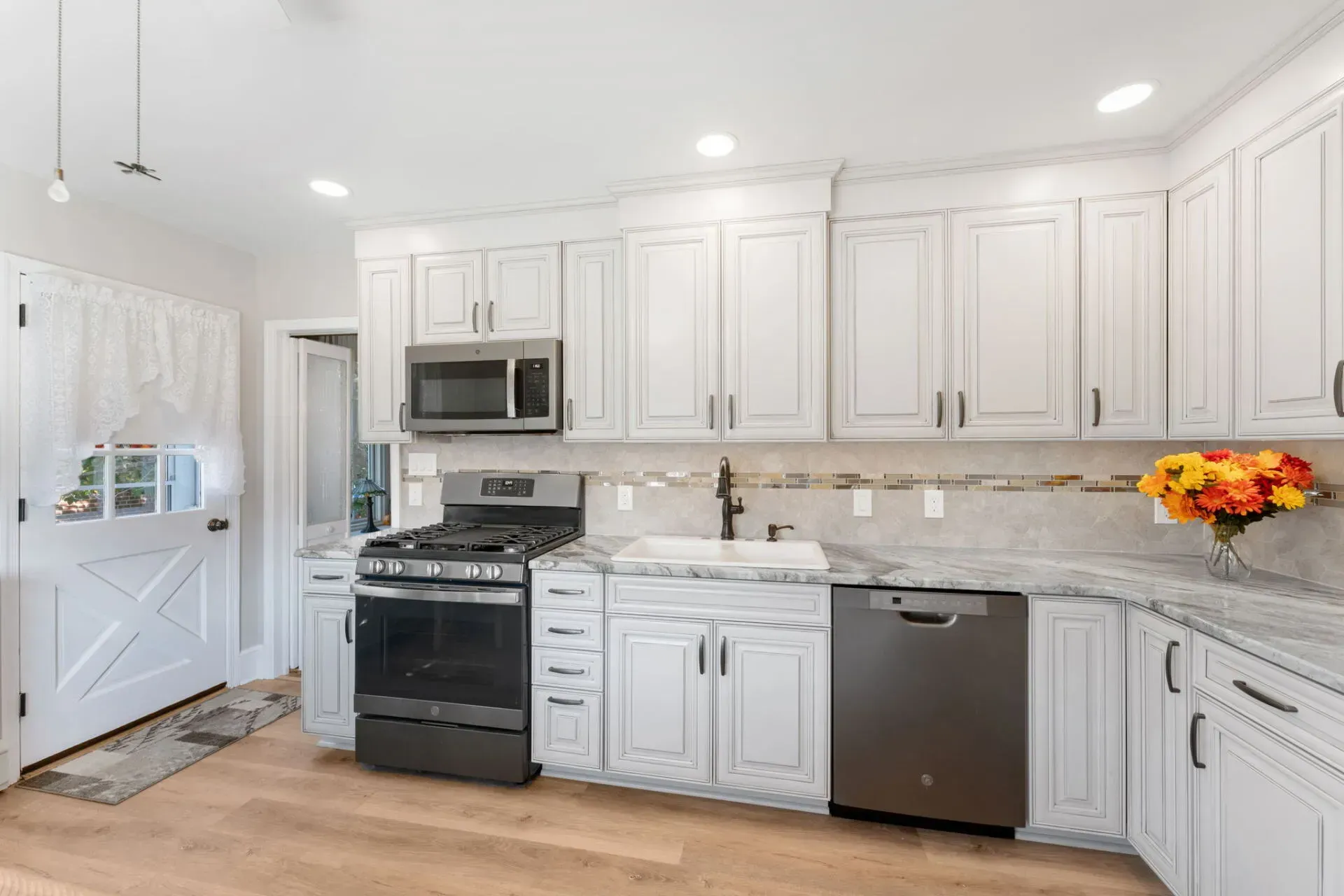 Bright white modern kitchen with stainless appliances, marble backsplash, and wood floor  In Bucks County PA