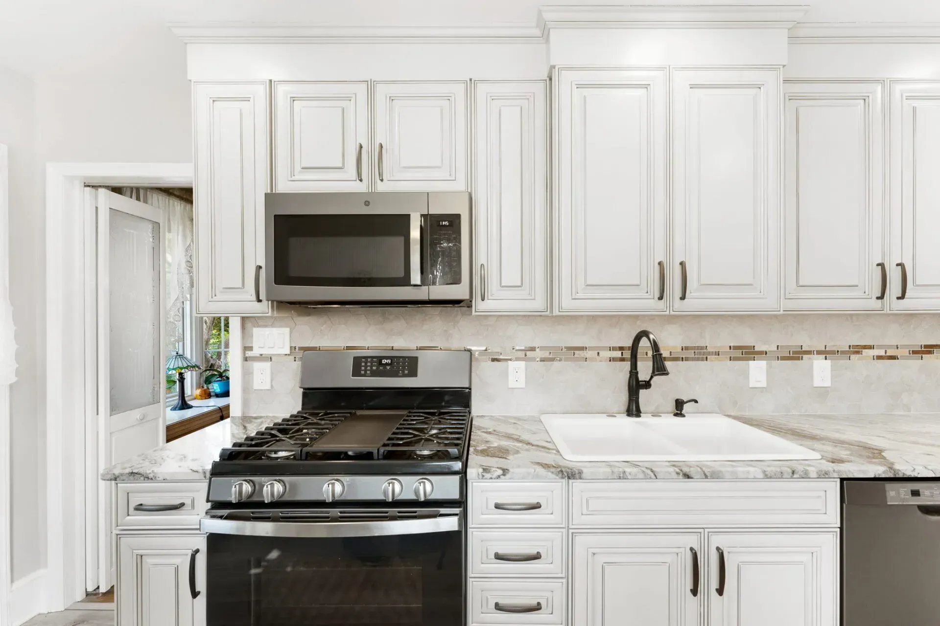 Bright white kitchen with stainless steel stove, microwave, cabinets, and marble countertops  In Bucks County PA