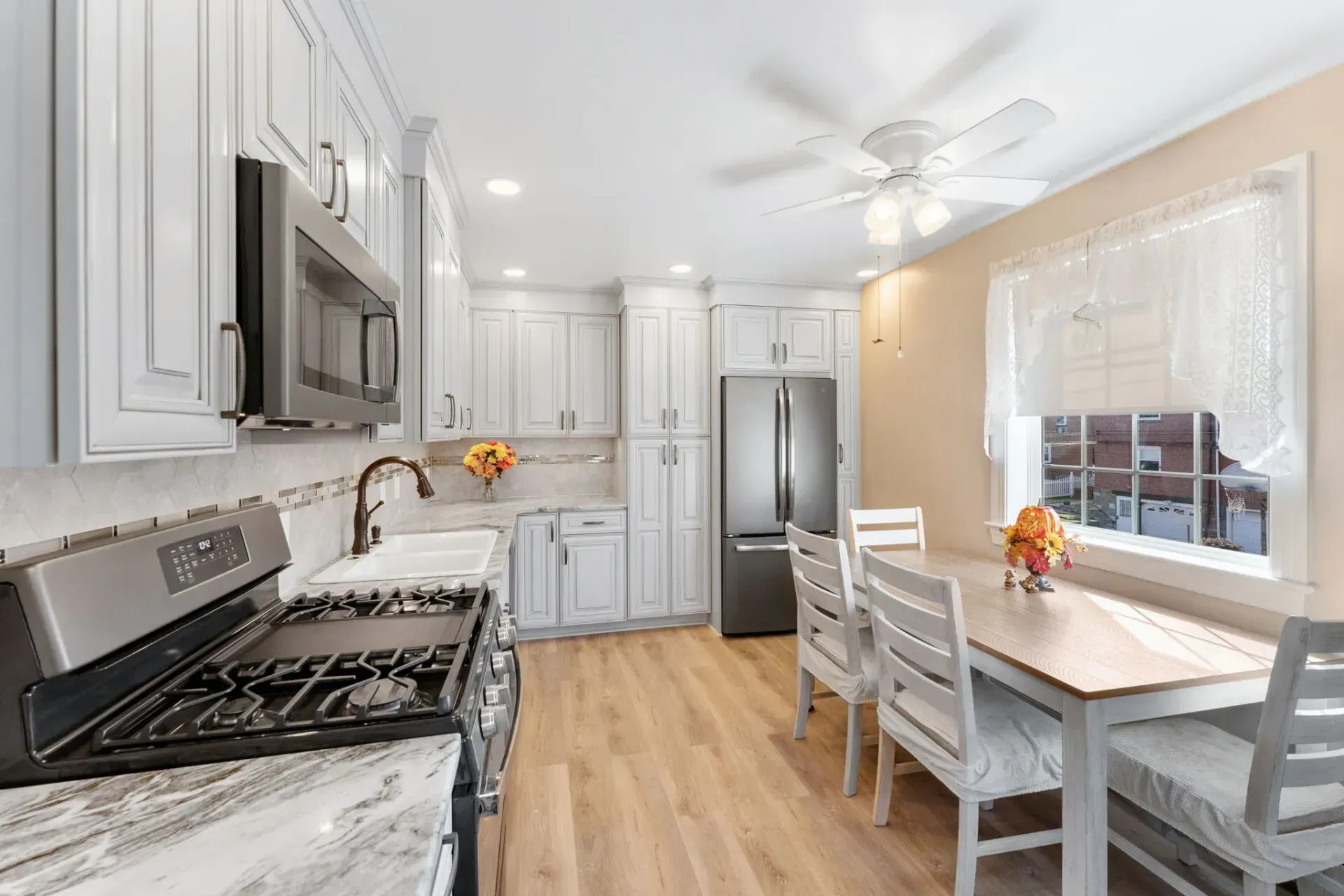 Bright white kitchen with stainless steel appliances, marble counters, and a small dining table by a window  In Bucks County PA