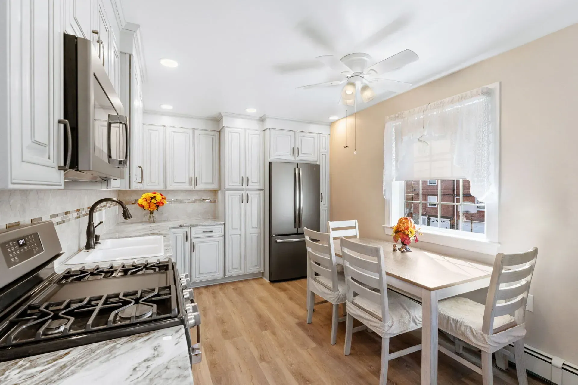 Bright white kitchen with stainless appliances, wood floor, and a dining table by a sunlit window  In Bucks County PA