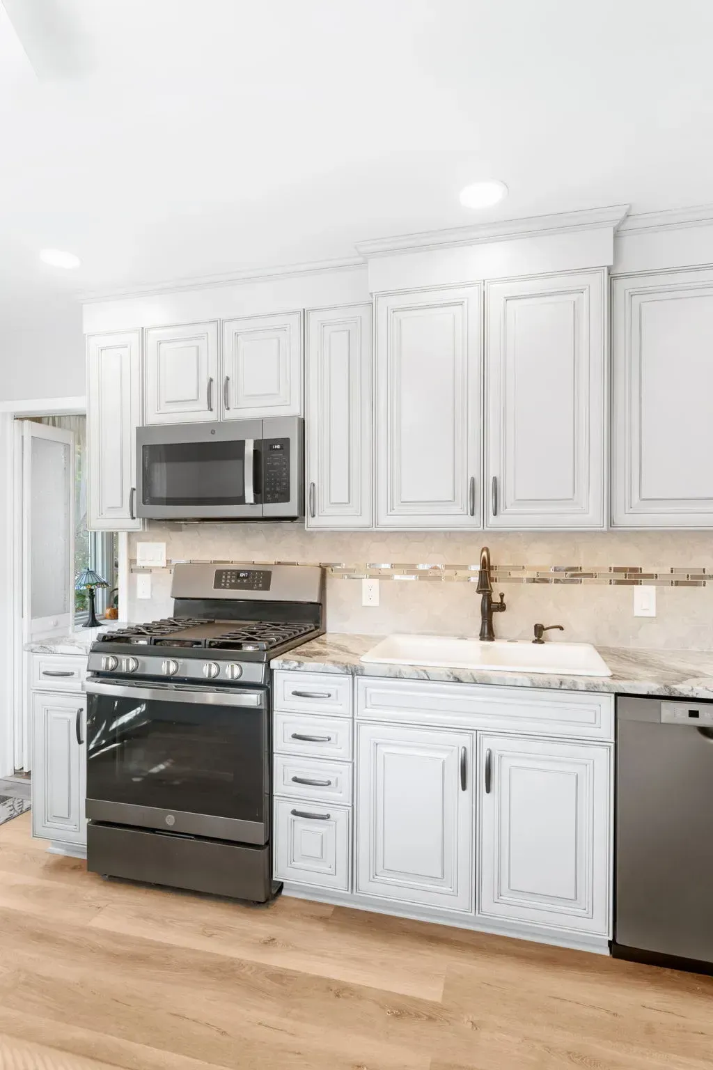 Bright white kitchen with stainless steel appliances, white cabinets, beige backsplash, and hardwood floor  In Bucks County PA