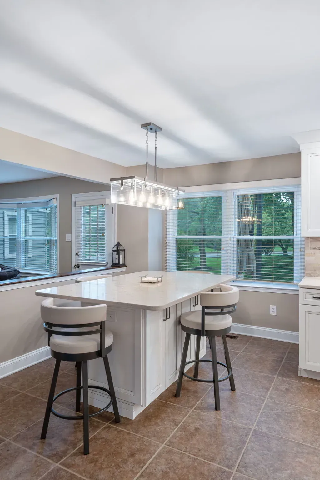 Bright kitchen with white island, pendant light, stools, and large windows overlooking greenery In Bucks Country PA
