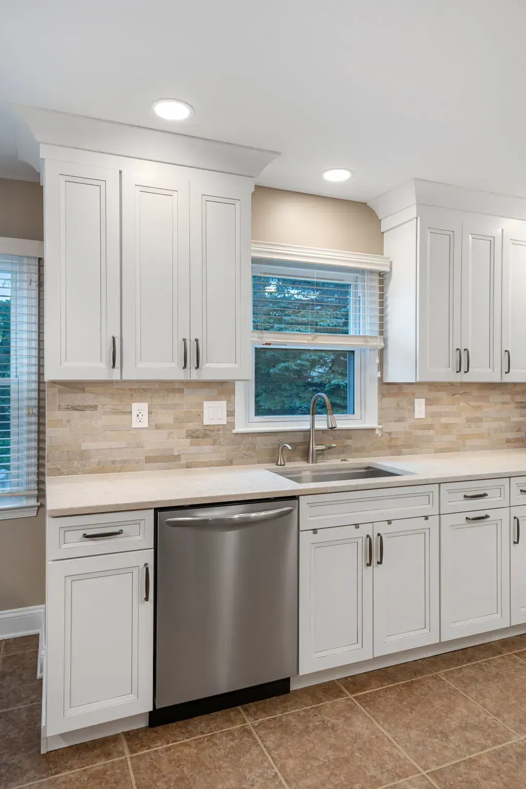 Modern white kitchen with stainless dishwasher, window over sink, and beige tile backsplash In Bucks Country PA