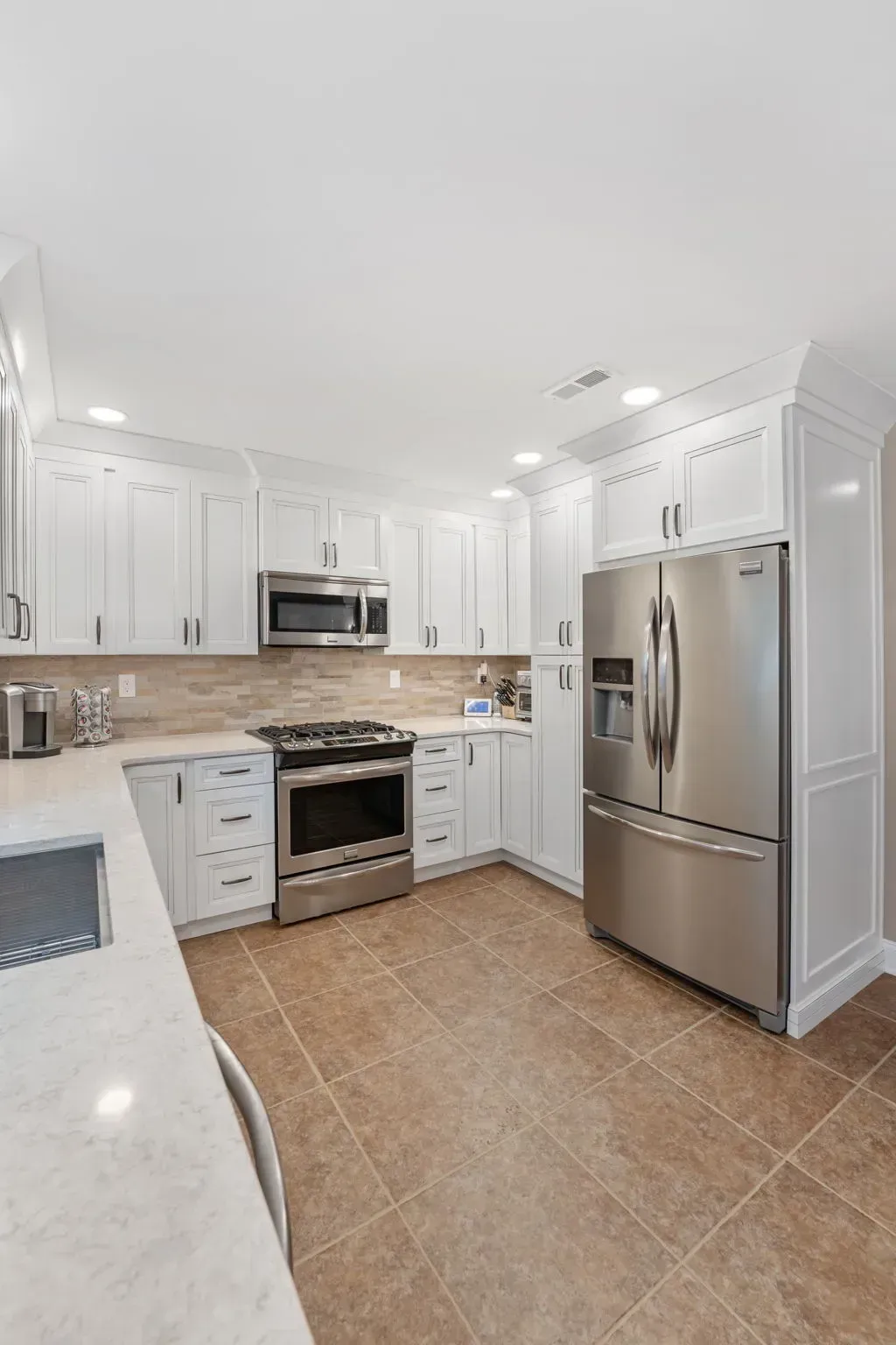 Bright white kitchen with stainless steel appliances, tan tile floor, and a large refrigerator In Bucks Country PA