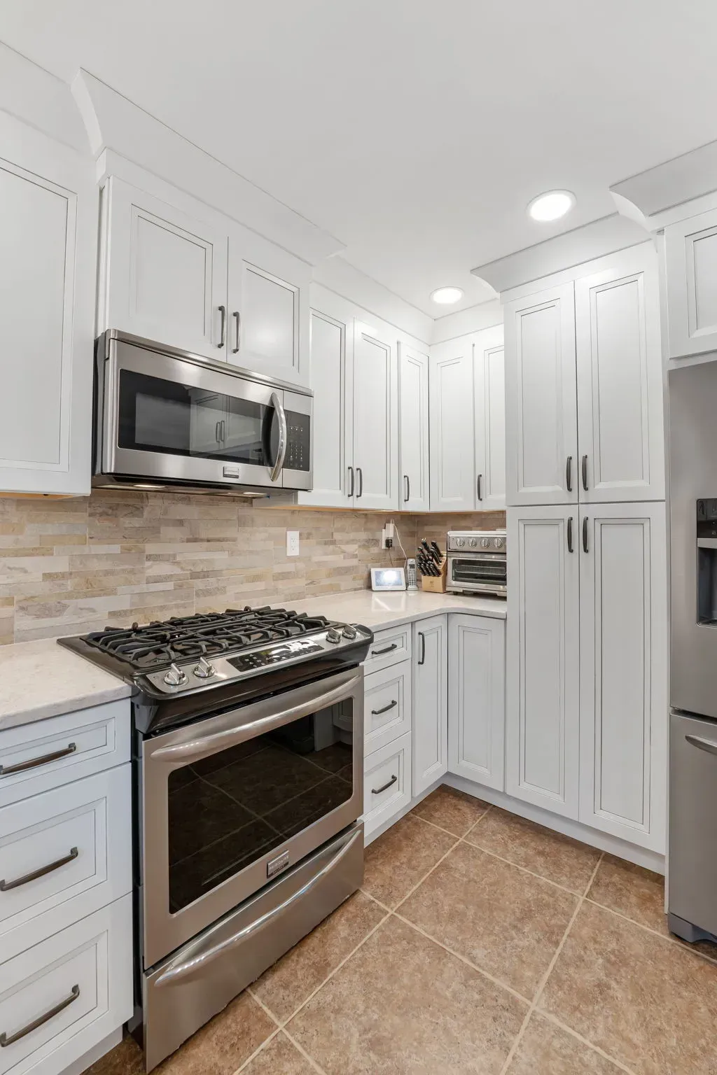 White modern kitchen with stainless steel stove, microwave, tall cabinets, beige tile backsplash and floor In Bucks Country PA
