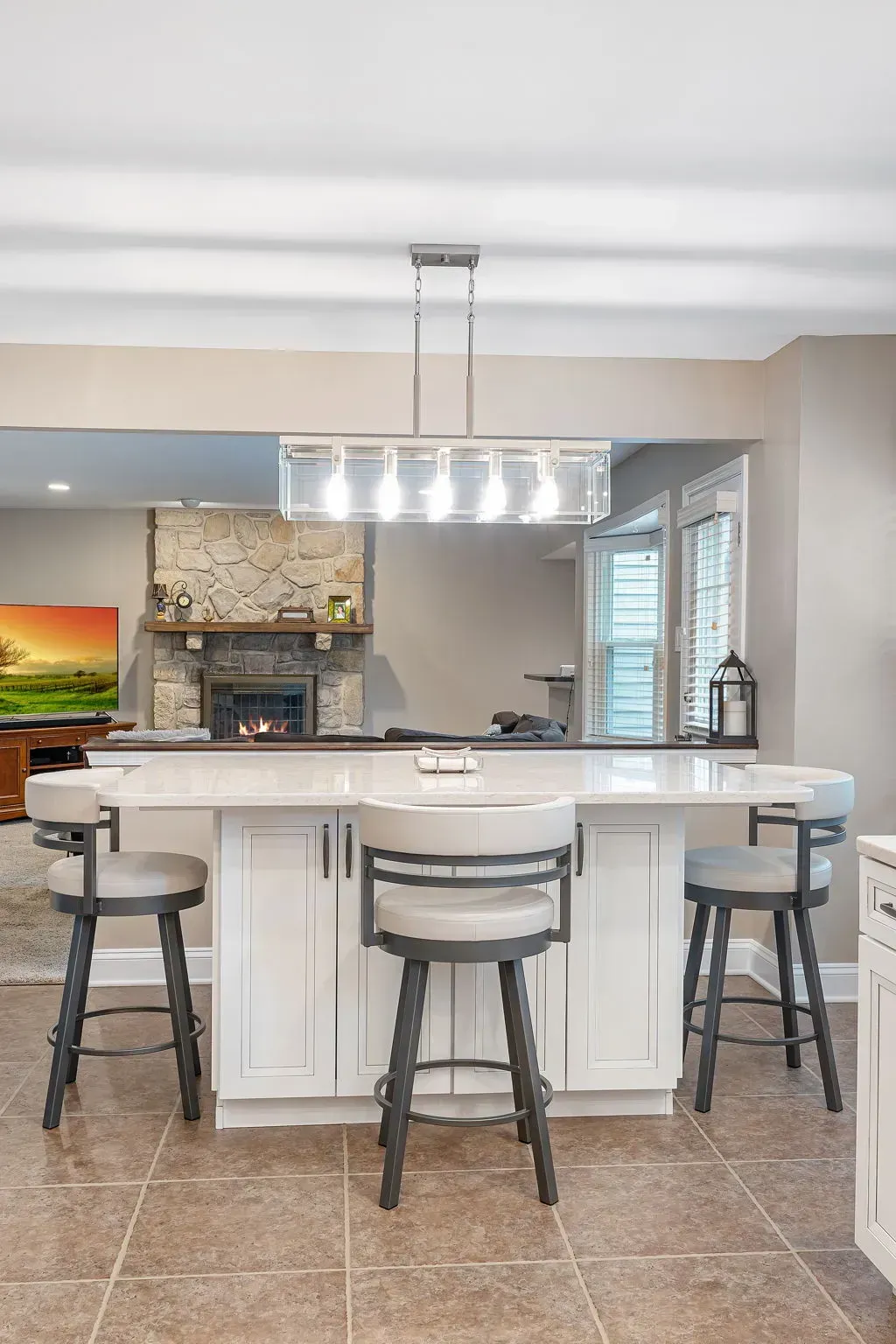 Modern kitchen with white island, three stools, stone fireplace, and pendant lights In Bucks Country PA