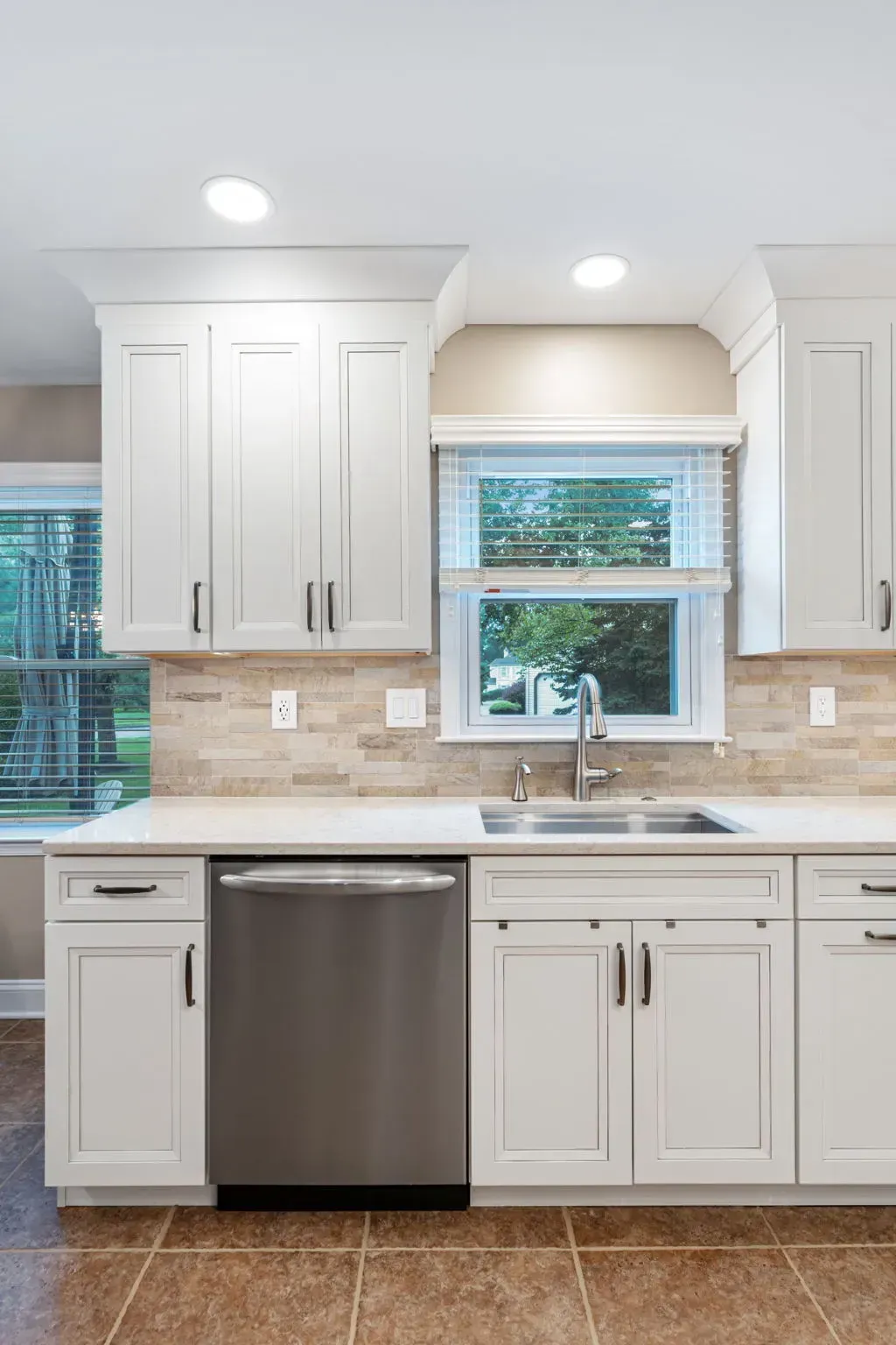 Bright white kitchen with stainless dishwasher, beige tile backsplash, and window over the sink In Bucks Country PA