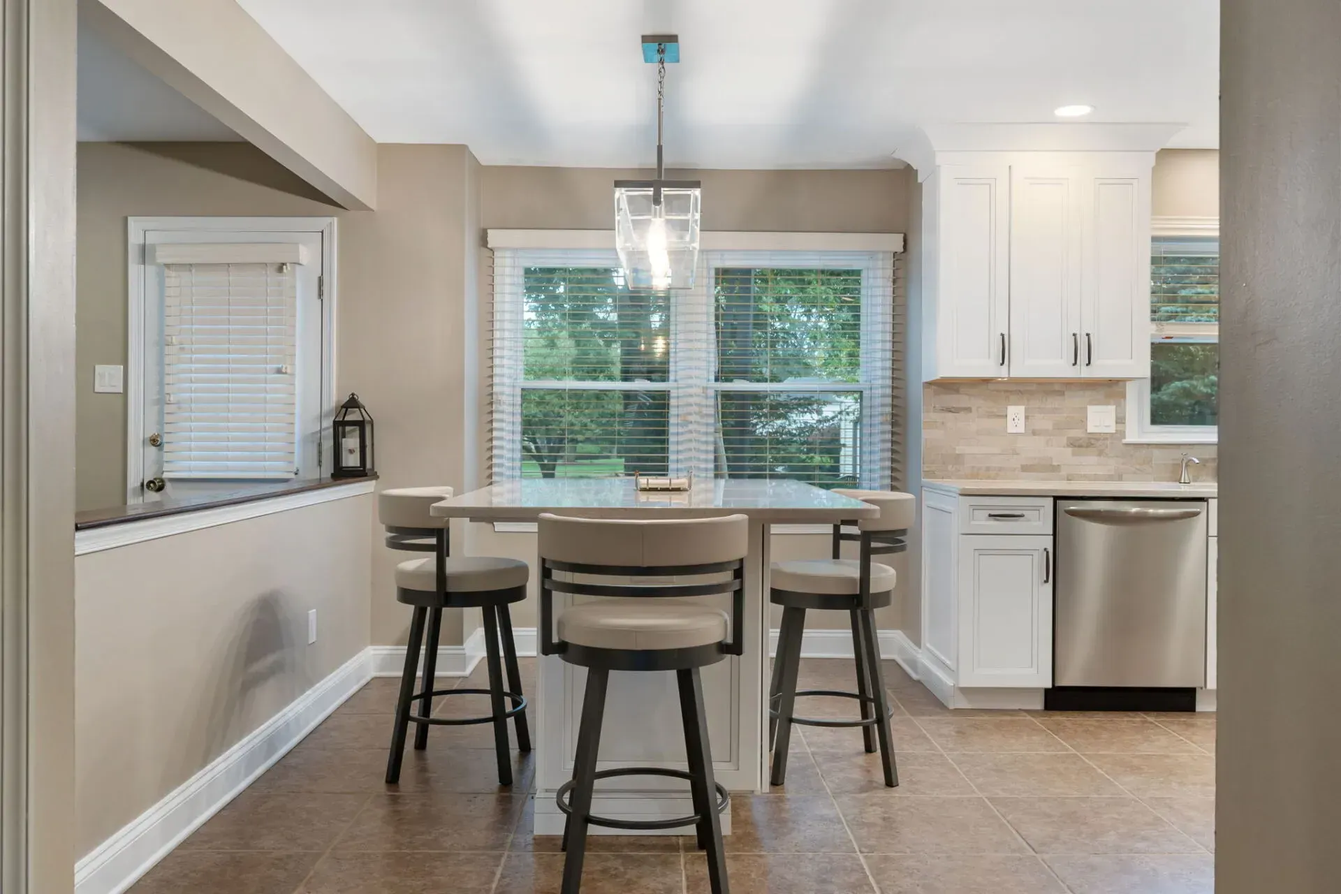 Modern kitchen and dining area with round table, bar stools, white cabinetry, and stainless steel appliances In Bucks County PA
