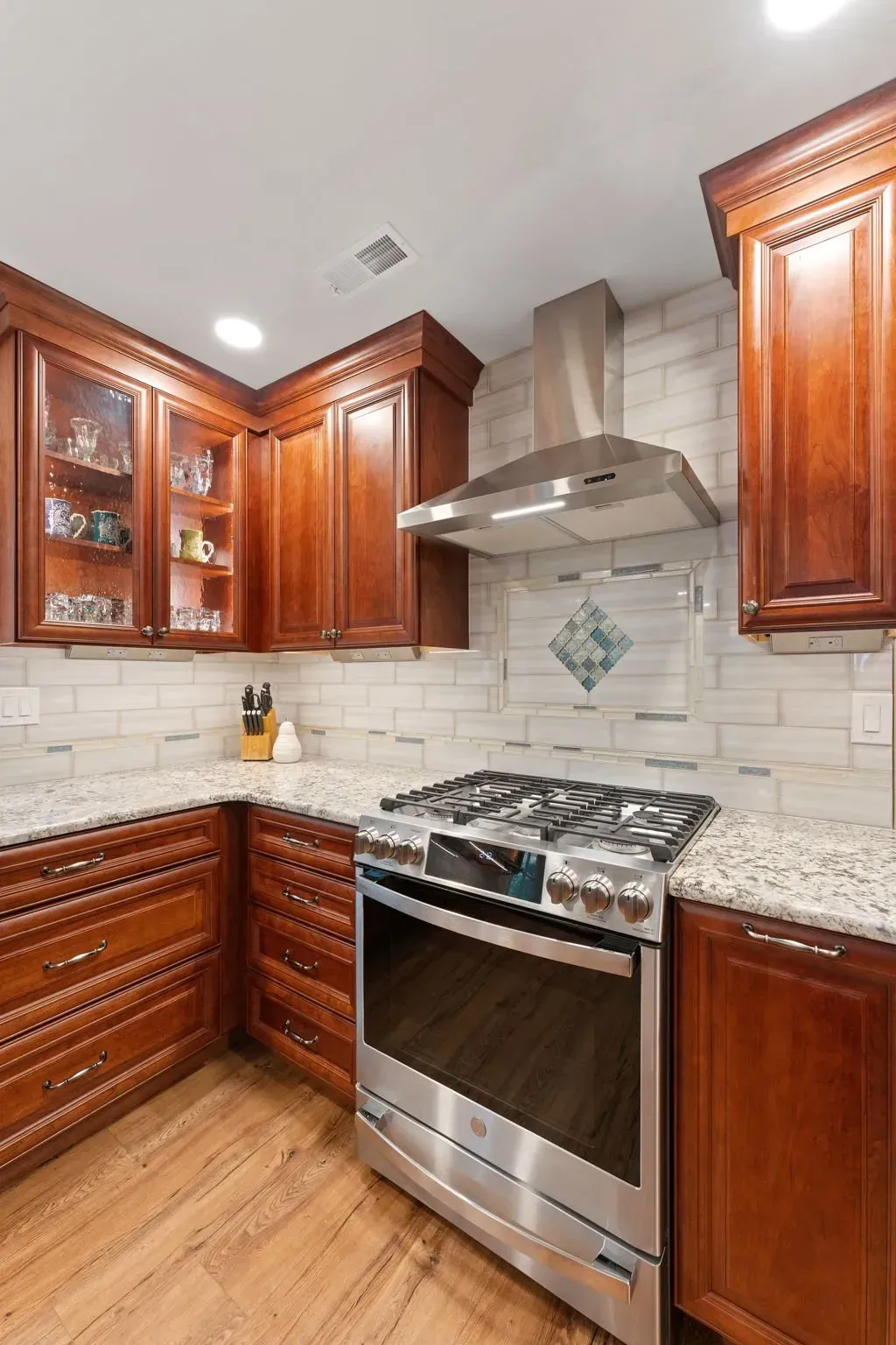 Modern kitchen with dark wood cabinets, stainless steel range hood, granite counters, and tile backsplash In Bucks Country PA