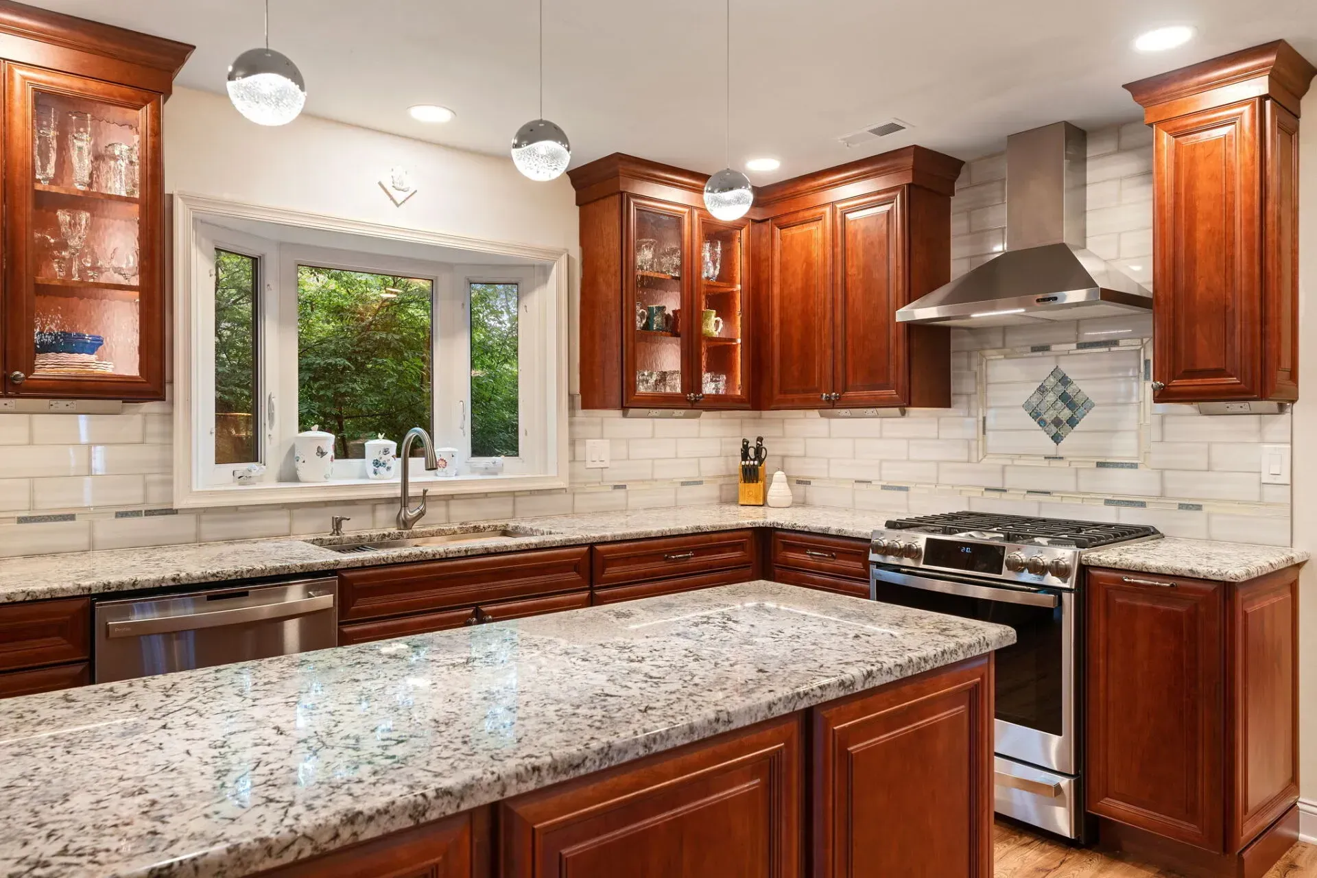 Bright kitchen with wood cabinets, granite island, white tile backsplash, and window over the sink In Bucks Country PA