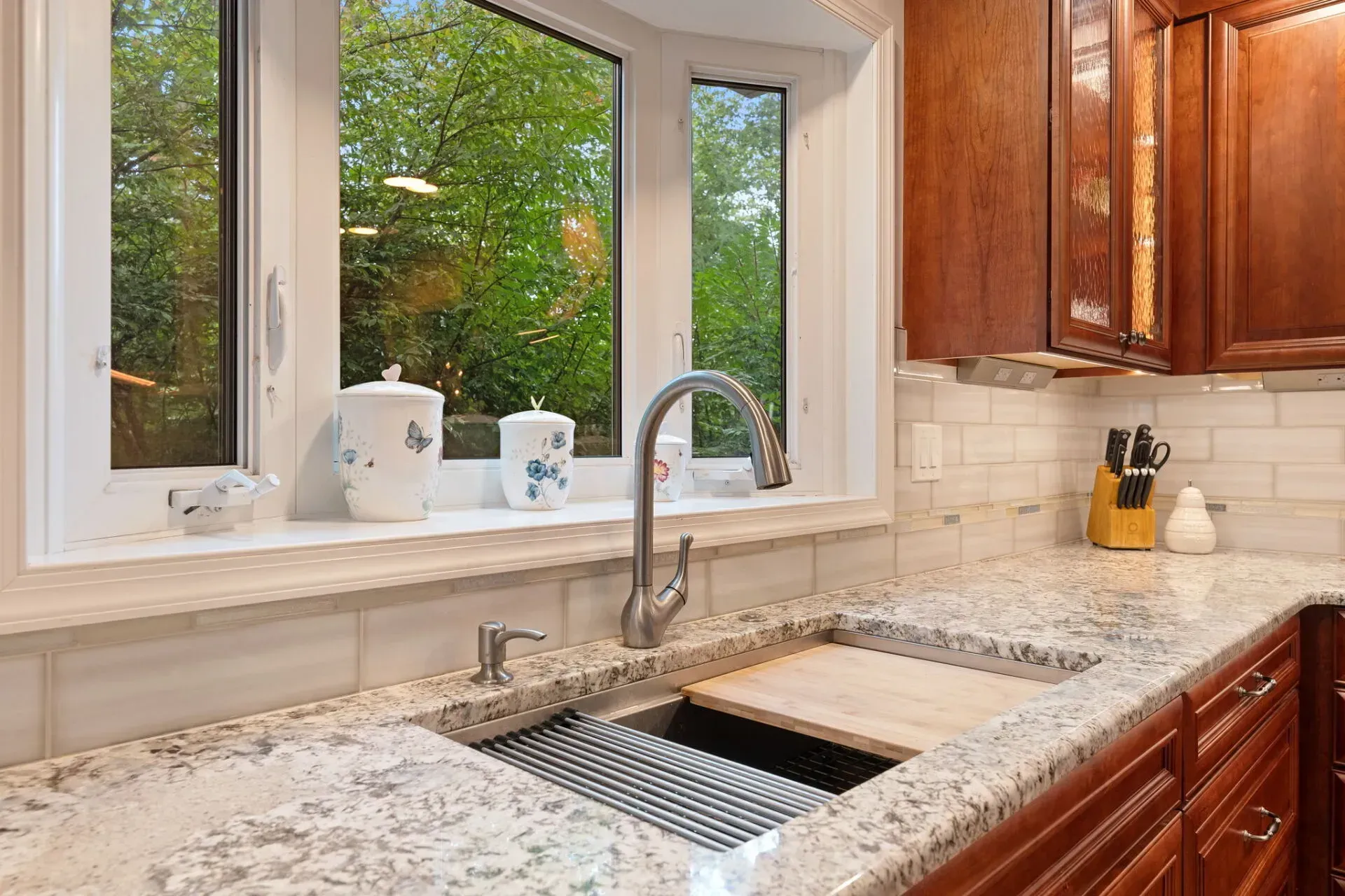 Kitchen sink under window with granite countertop, chrome faucet, and wooden cabinets In Bucks Country PA