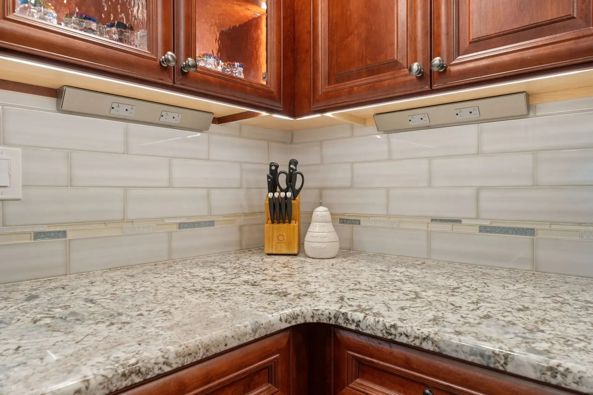Corner kitchen countertop with granite surface, white tile backsplash, wood cabinets, and knife block In Bucks Country PA