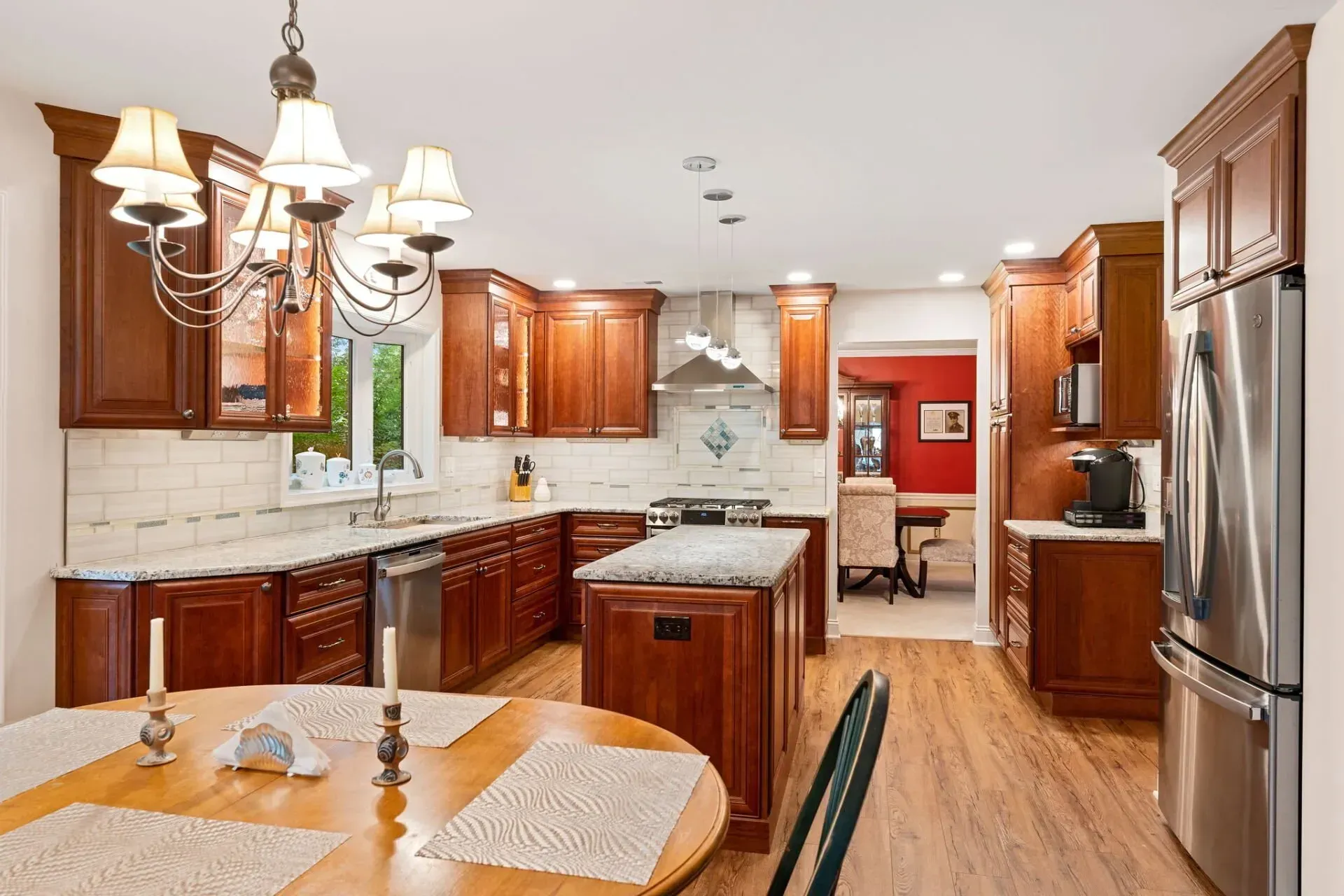 Bright kitchen with wooden cabinets, stainless fridge, island, dining table, and chandelier
