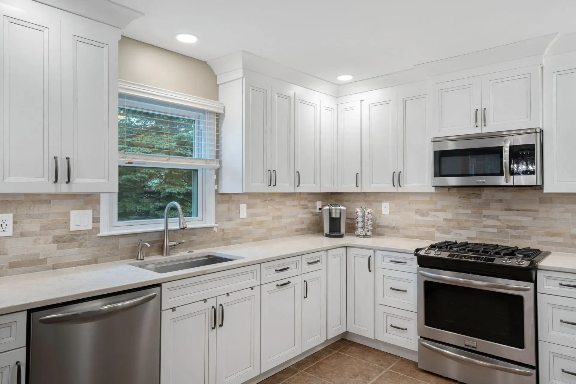 Bright white kitchen with stainless steel appliances, beige tile floor, and a window above the sink. In Bucks County PA