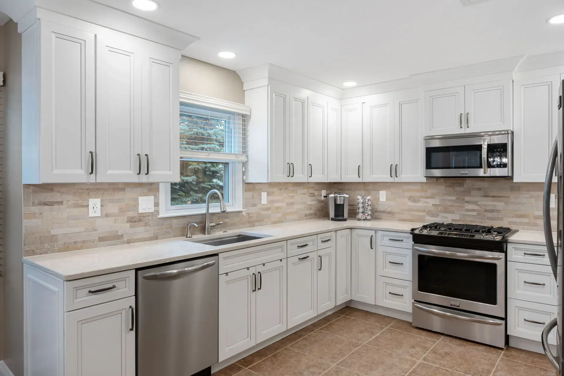 Bright modern white kitchen with stainless steel appliances, marble countertops, and beige tile floor  In Bucks County PA