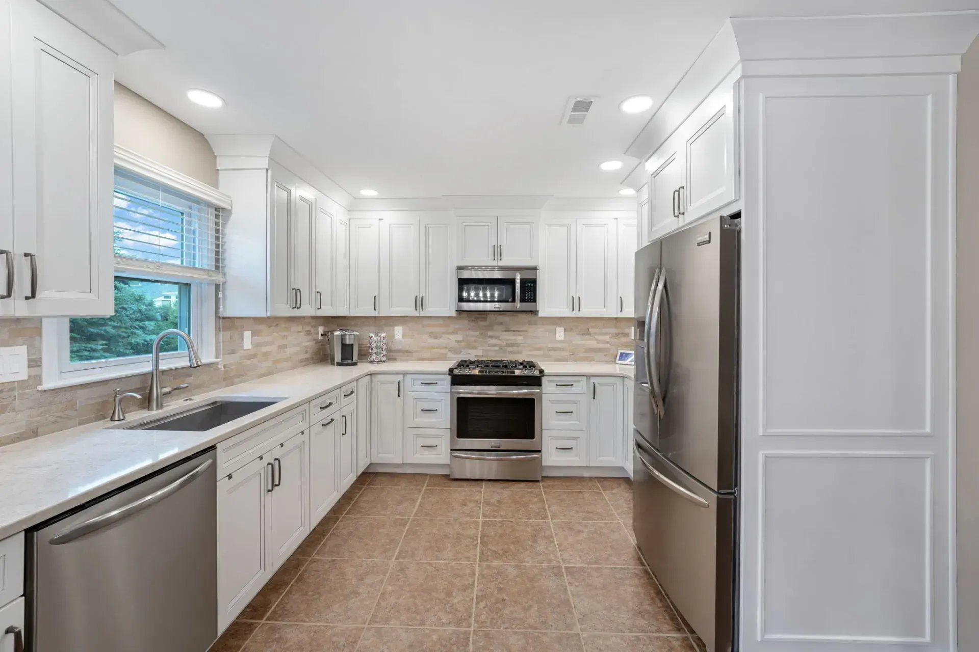 Bright white kitchen with stainless steel appliances, tan tile floor, and large window over the sink  In Bucks County PA