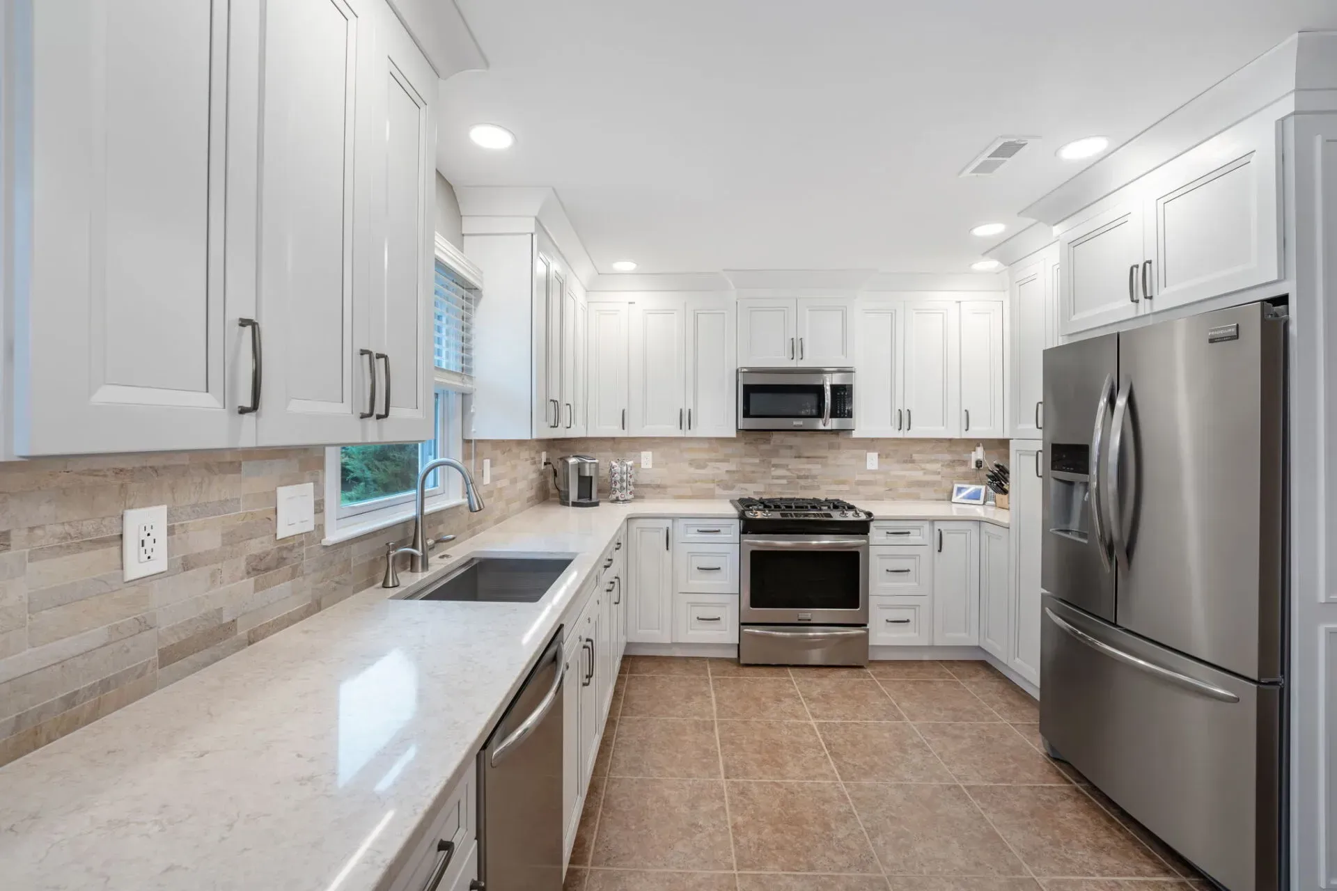 Bright white modern kitchen with stainless steel appliances, granite counters, and tan tile flooring  In Bucks County PA